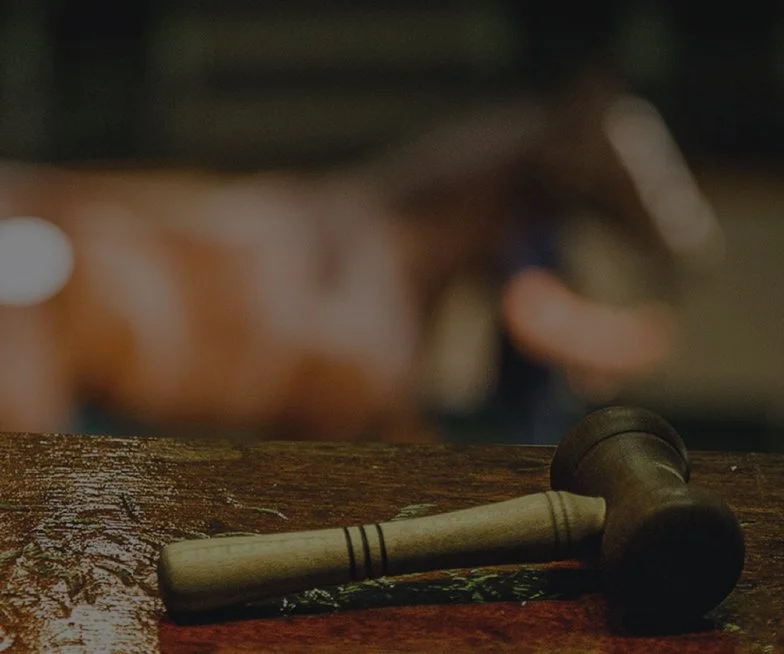A wooden mallet resting on a dark wooden surface with a blurred horse statue in the background.