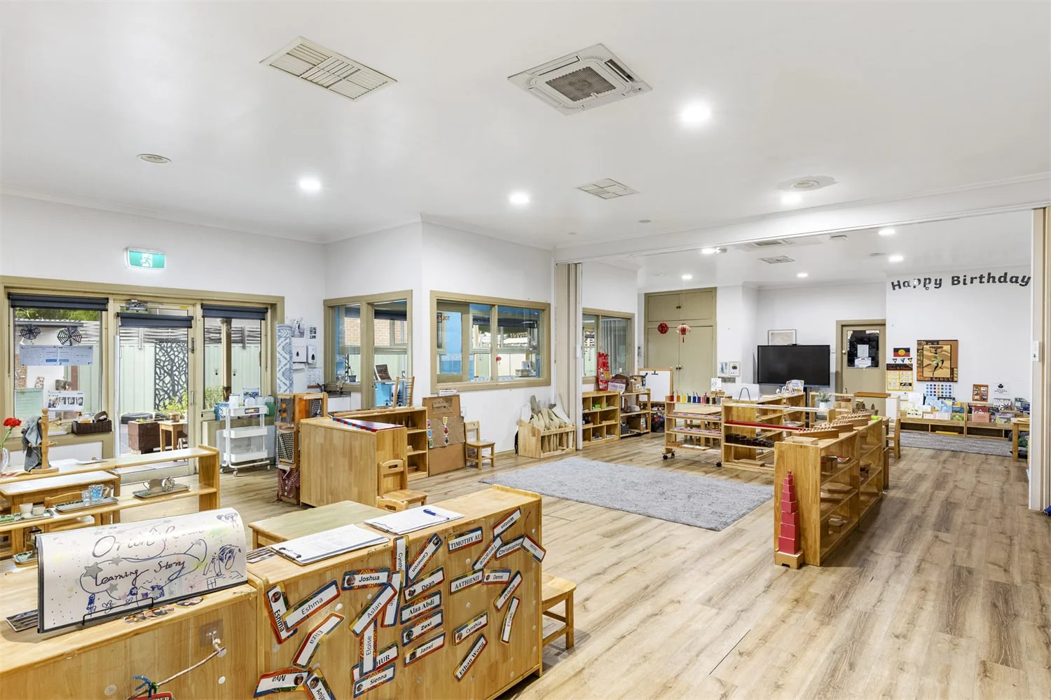 A spacious classroom with wooden furniture, educational materials, windows, and a 