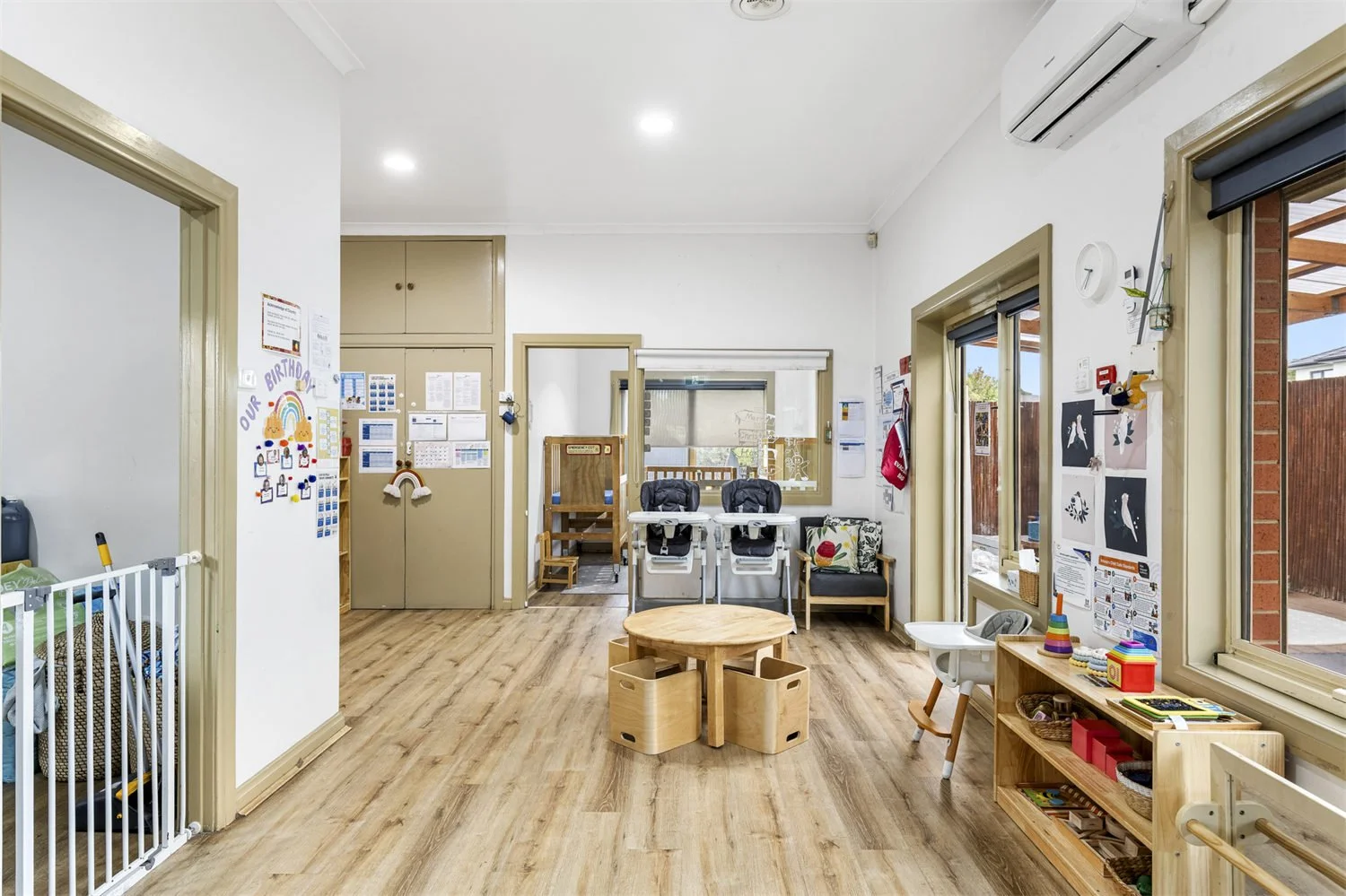 An empty children’s playroom with wooden floors, decorated walls, children's furniture, and toys.