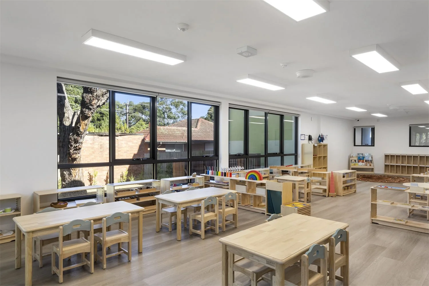 Bright, spacious classroom with large windows, light wooden furniture, and educational materials for young children.