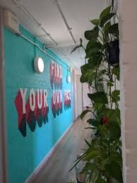 Colorful wall with motivational text in a hallway, with a tall plant beside it.