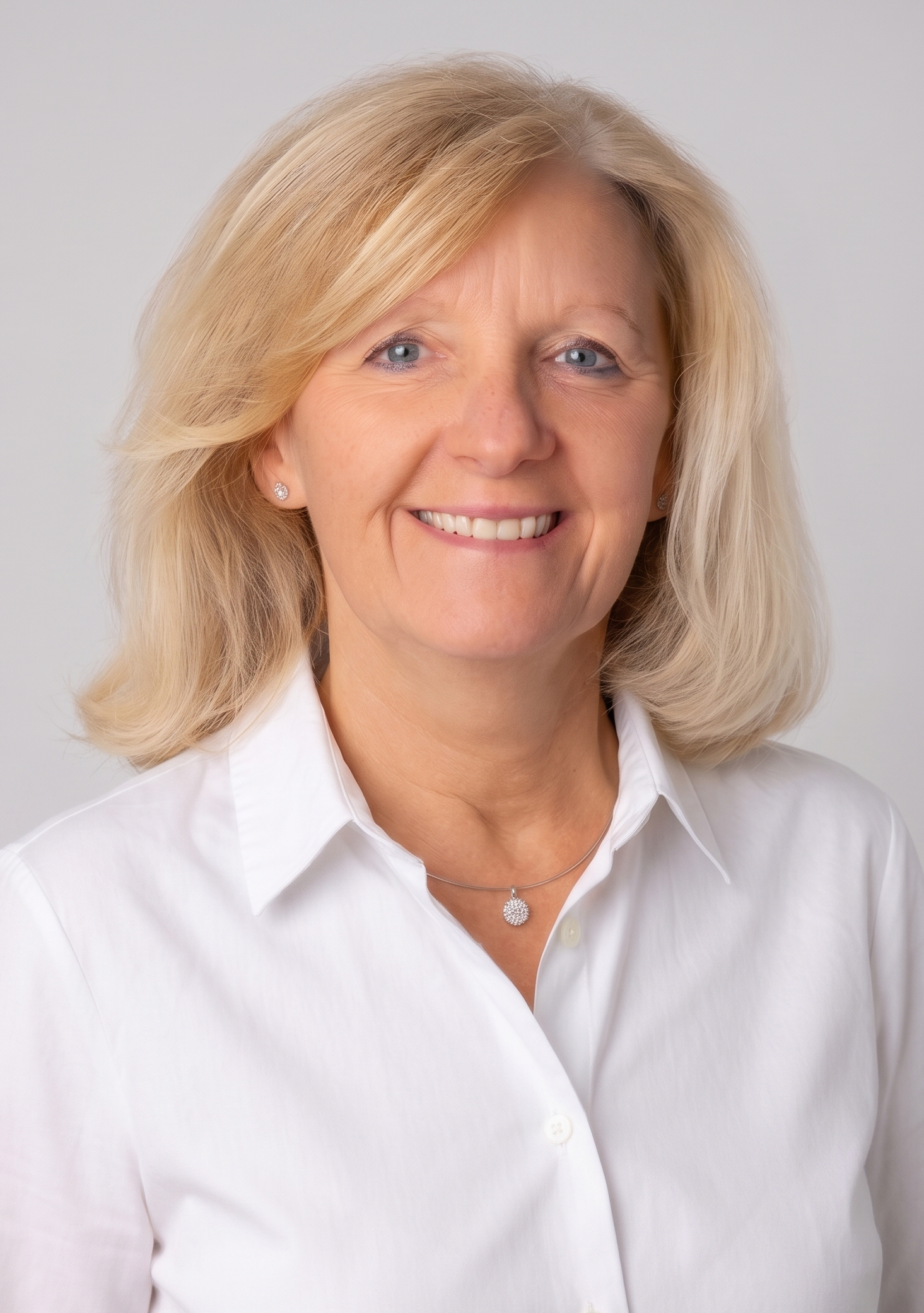 Porträt eines lachenden, smiling älteren Frau mit blondem Haar, weiße Bluse, silberne Schmuck, gegen weißen Hintergrund.