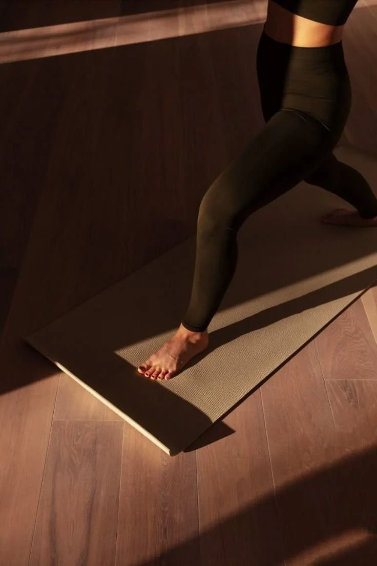 Person in schwarzer Yogahose macht Yoga auf einer Matte auf Holzboden.