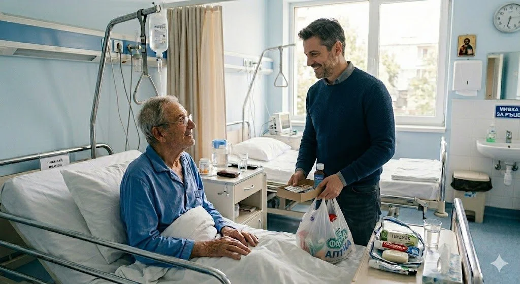 A man in a dark sweater is smiling and handing a shopping bag to an elderly man in a hospital bed. The elderly man is sitting up, wearing glasses and a blue hospital gown. The hospital room has two beds, medical equipment, and a window with sunlight streaming in.