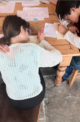 Two children, a girl and a boy, are working together at a wooden table with various papers and notebooks.