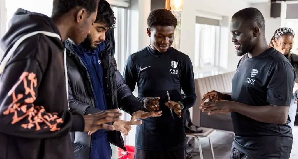A group of young men playing a game on a smartphone in a casual indoor setting.