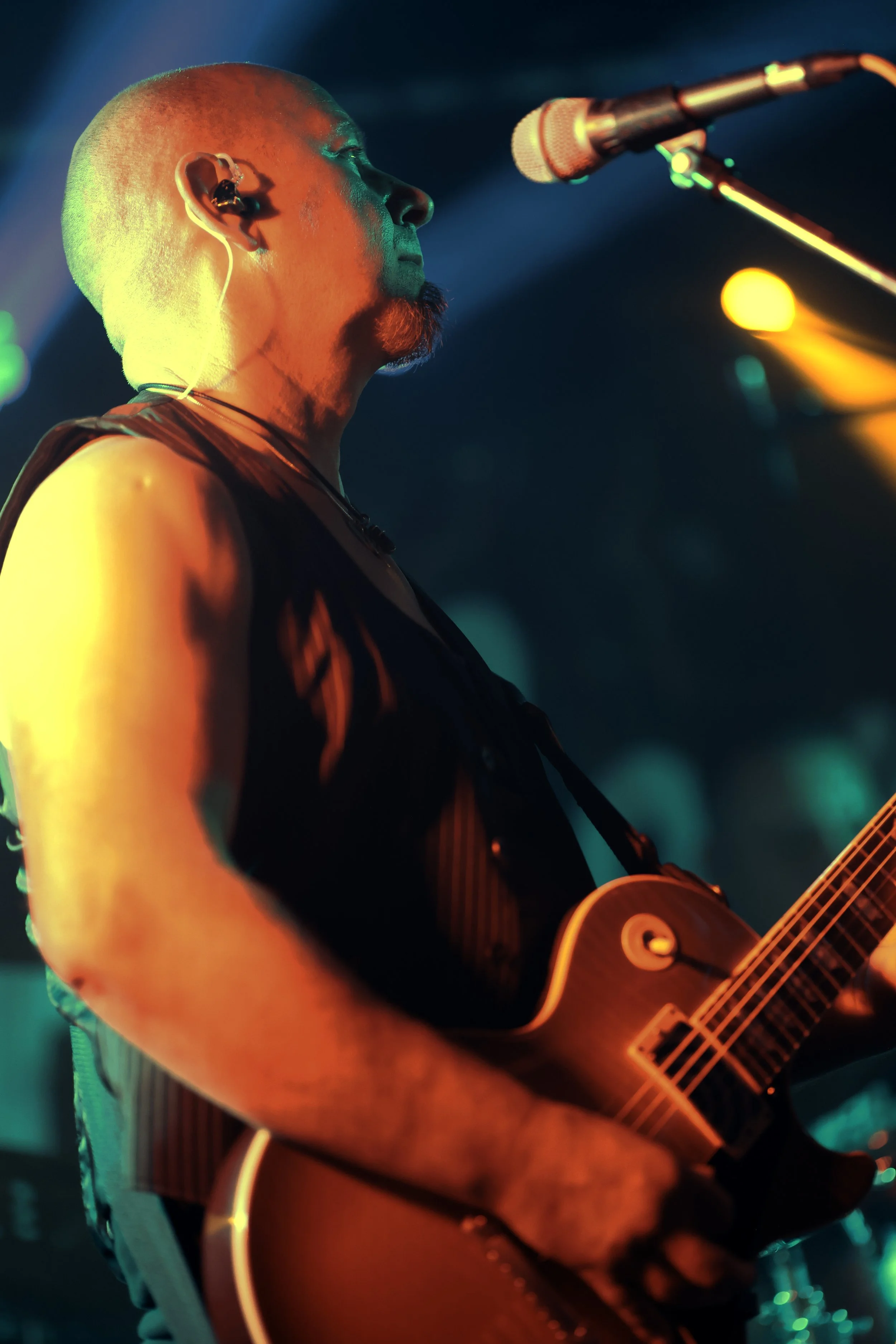 A person playing guitar on stage, illuminated by colorful stage lights, showing a focused expression.