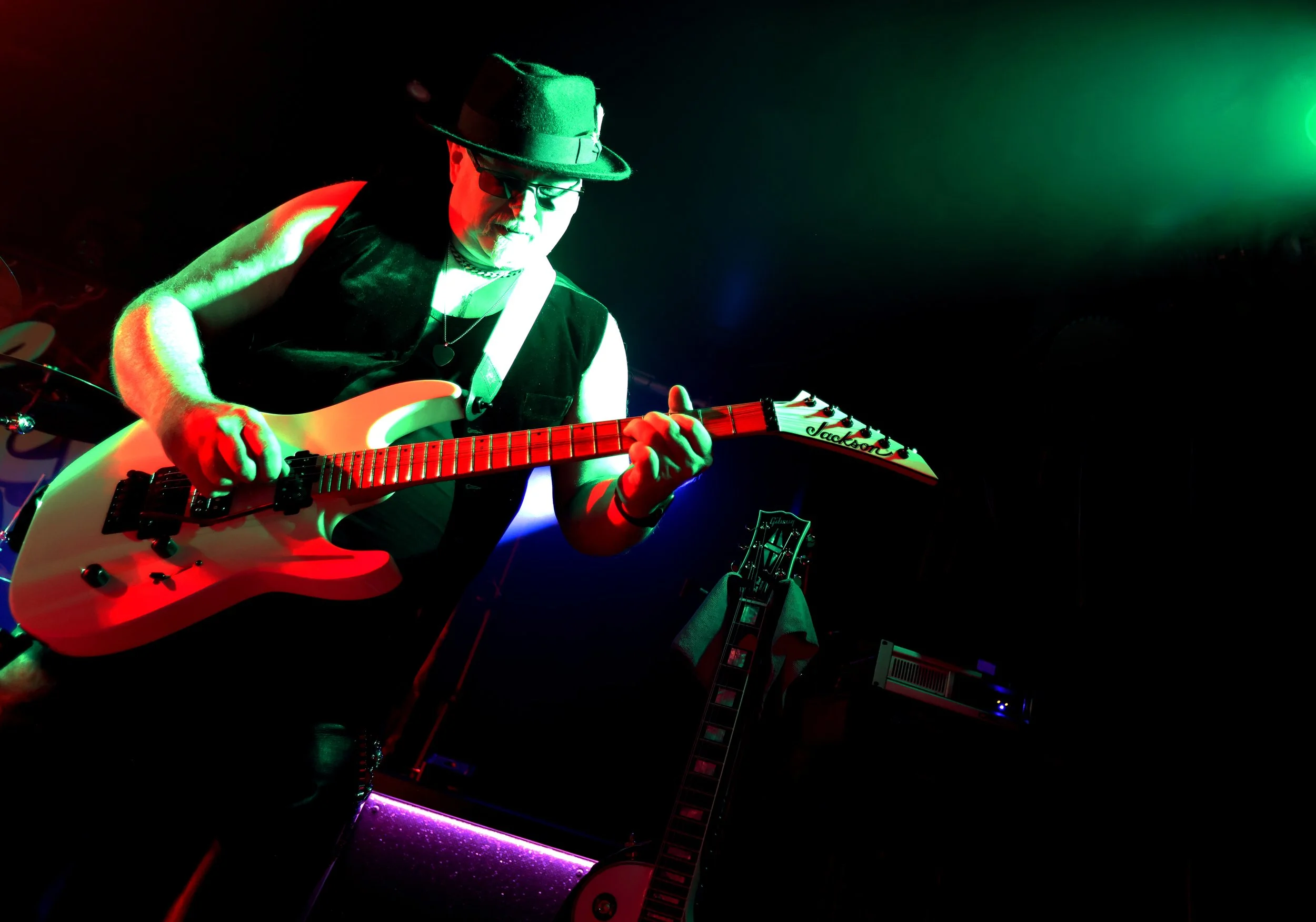 A person playing an electric guitar on stage with colourful stage lighting in red, green, and purple.