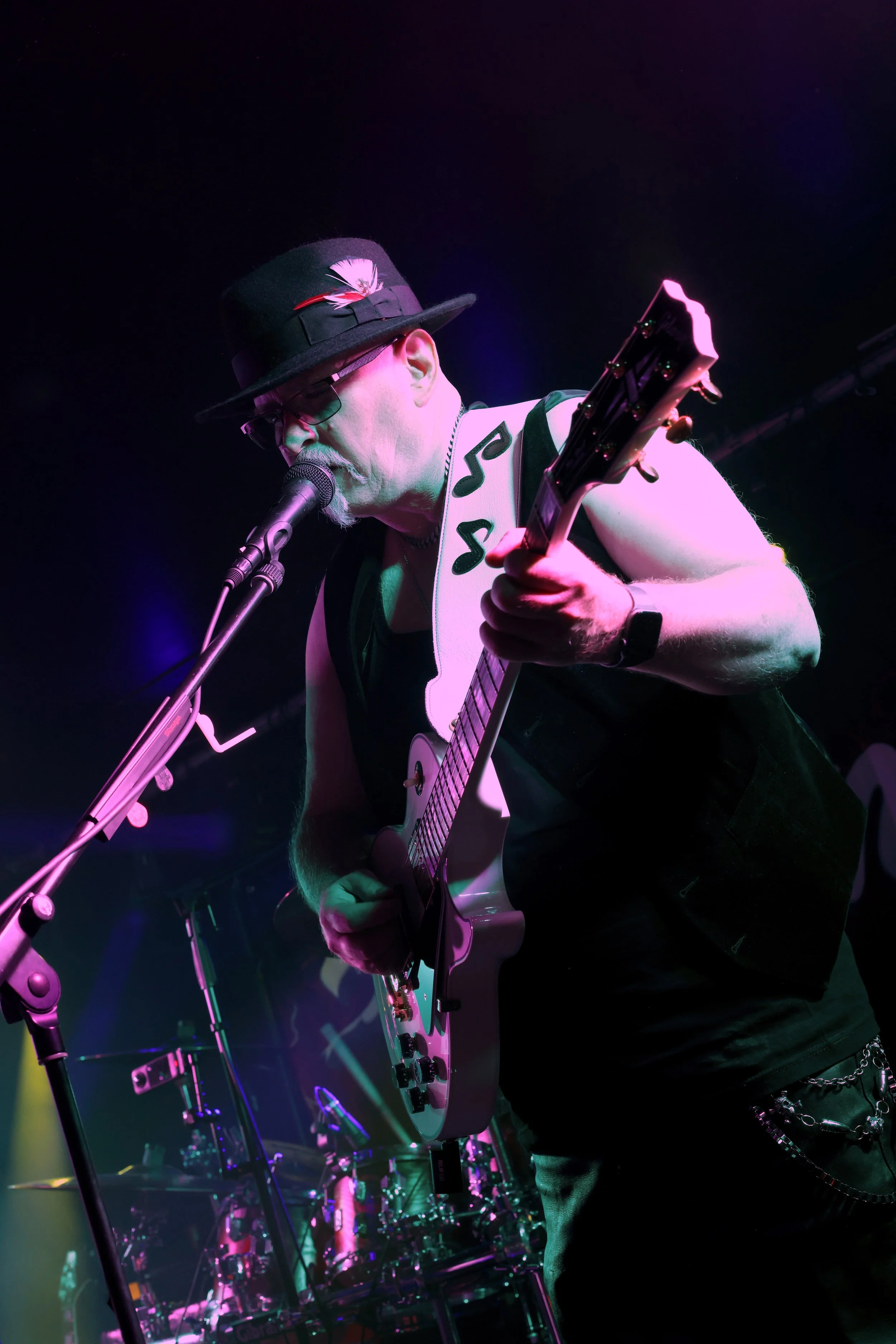 Music performer playing guitar and singing into microphone on stage with colourful lights.