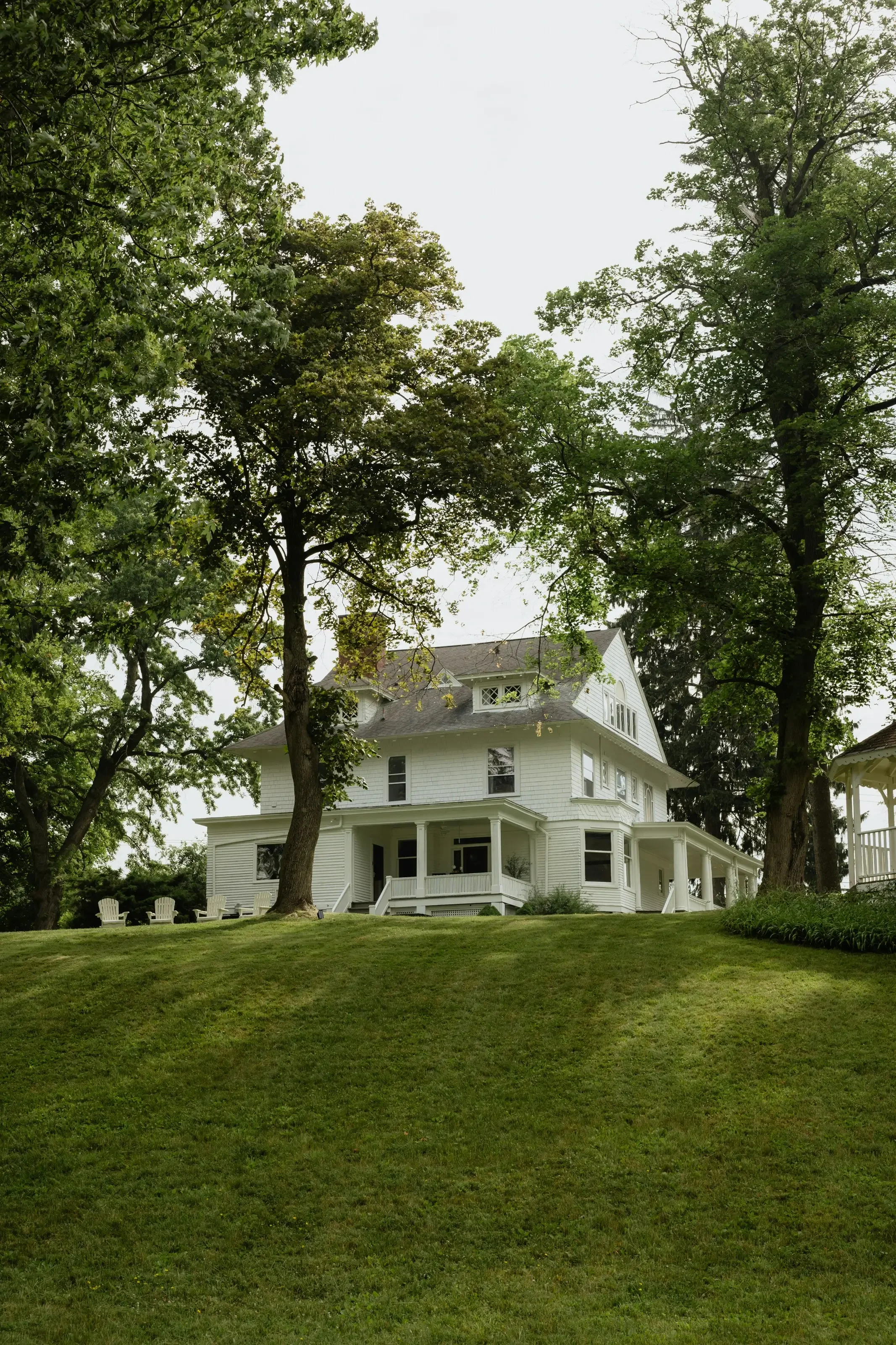 Large white Victorian-style house with a wrap-around porch, surrounded by tall trees and a well-manicured lawn.