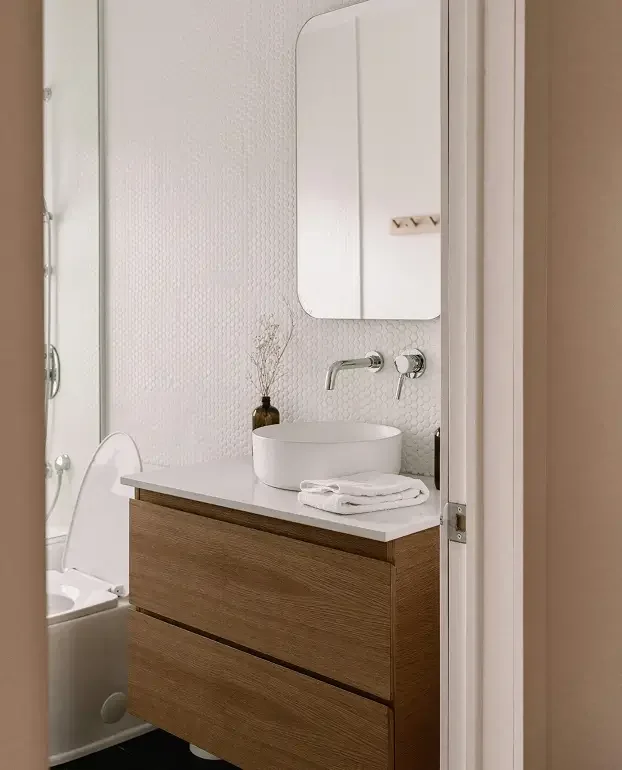 Modern bathroom with white textured wall, oval vessel sink on a wooden vanity, mirror, and a small vase with dried plants.