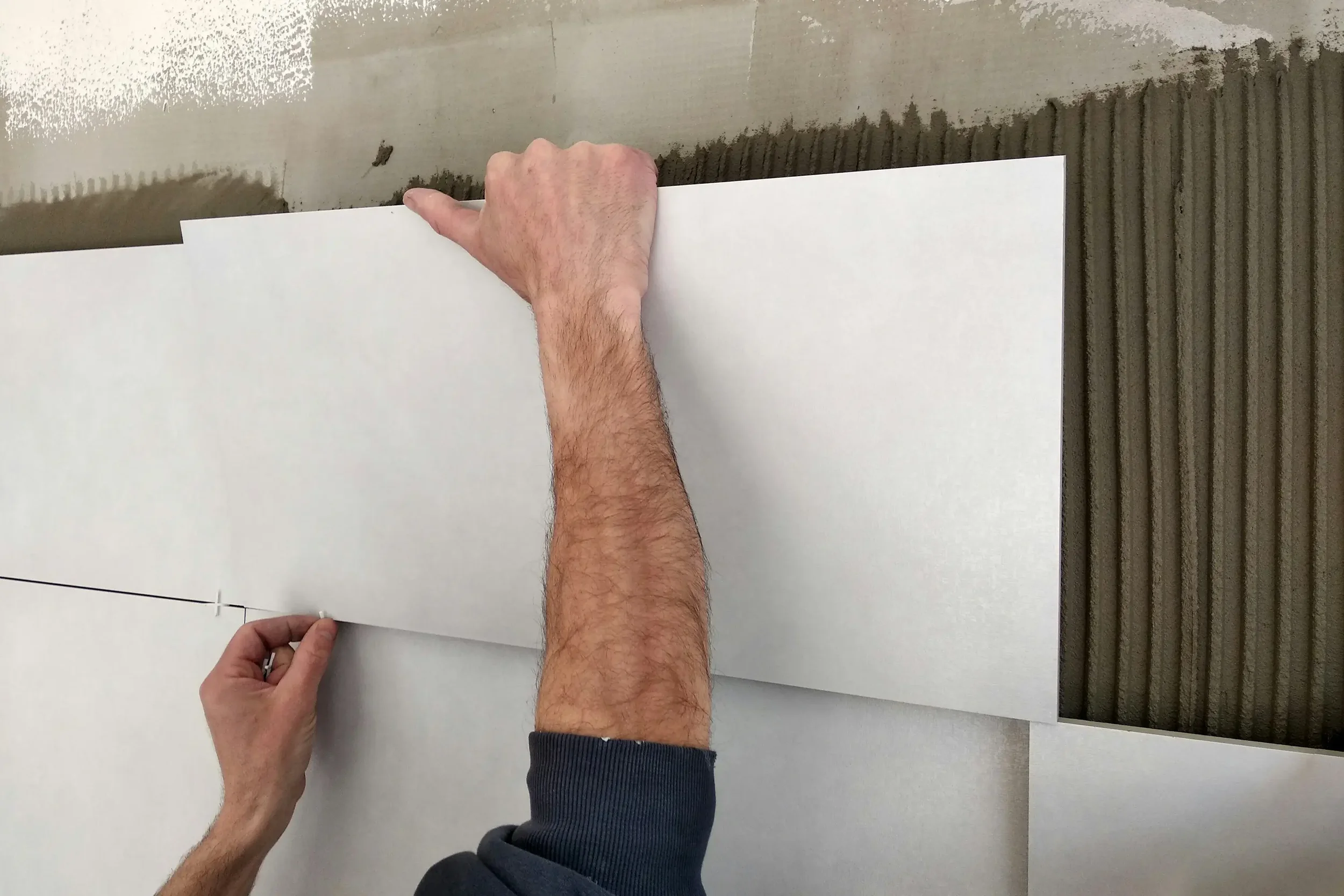 Person installs white ceiling tiles in a grid ceiling framework.