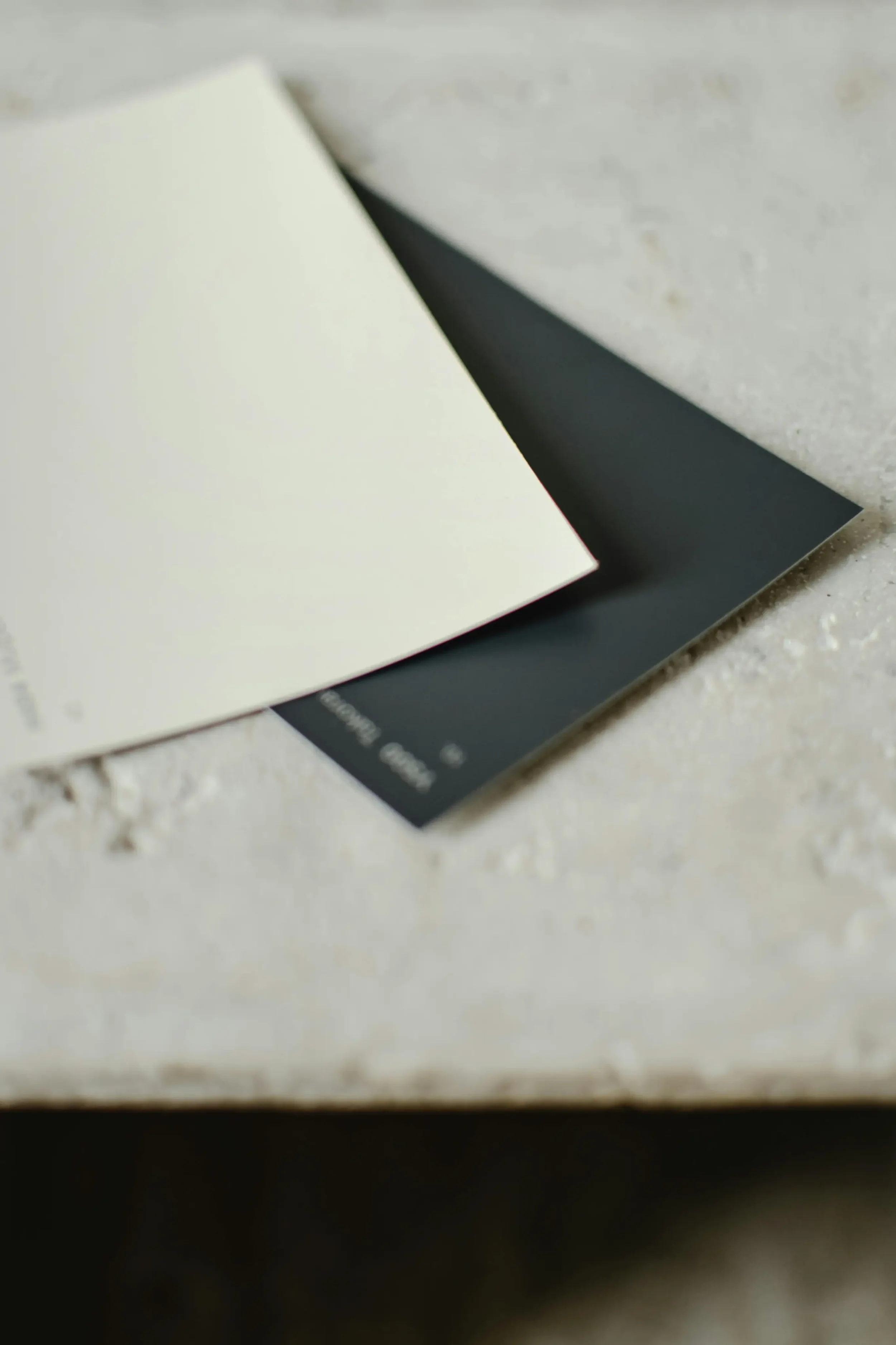 Two overlapping color swatches, one off-white and one dark gray, on a textured surface.