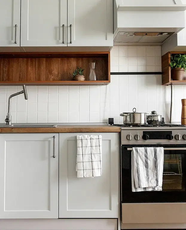 Kitchen with white cabinets, wooden open shelves, a stainless steel stove with pots, a window, a white tiled backsplash, and a small potted plant.