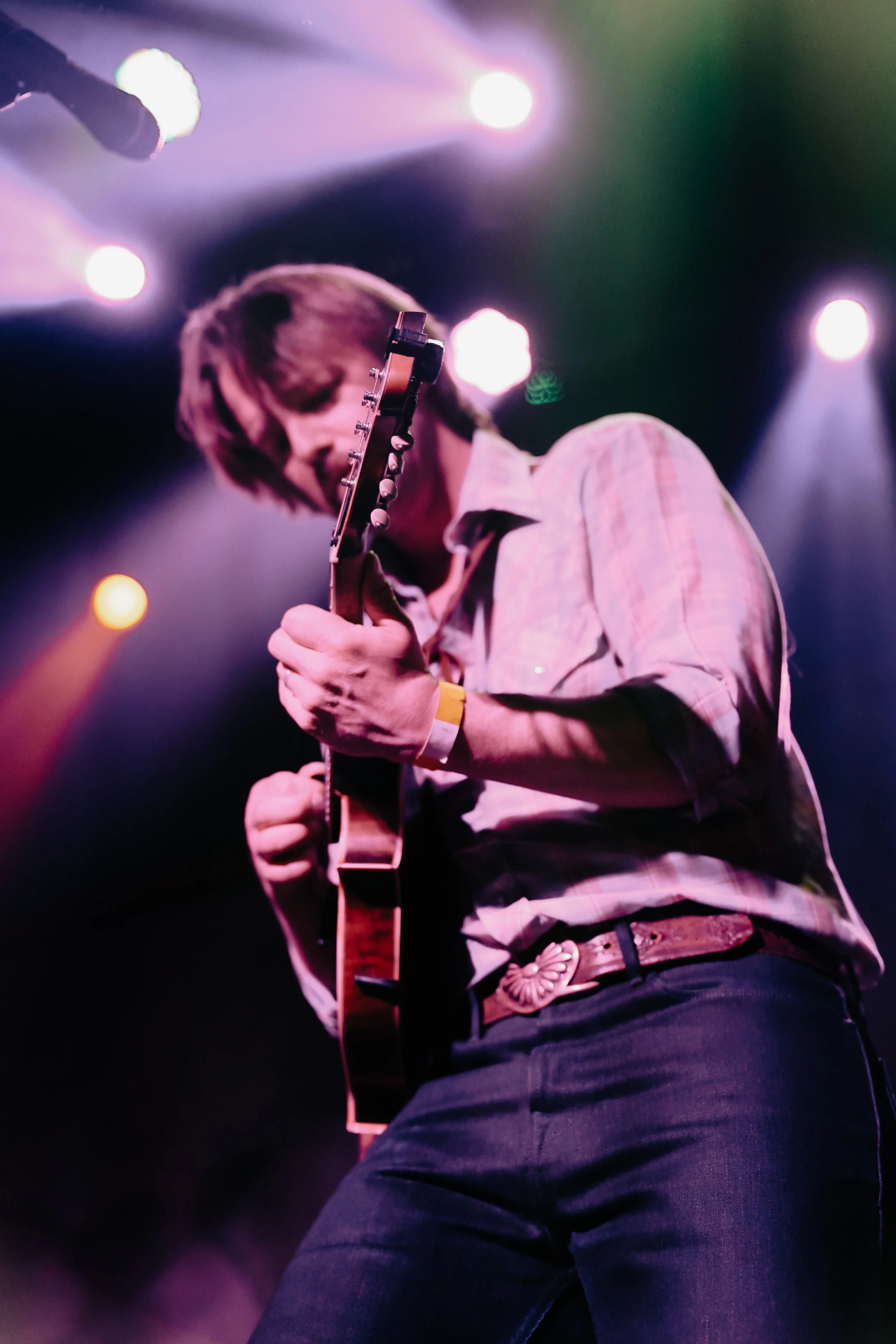 Person playing an electric guitar on a stage with colorful stage lights.