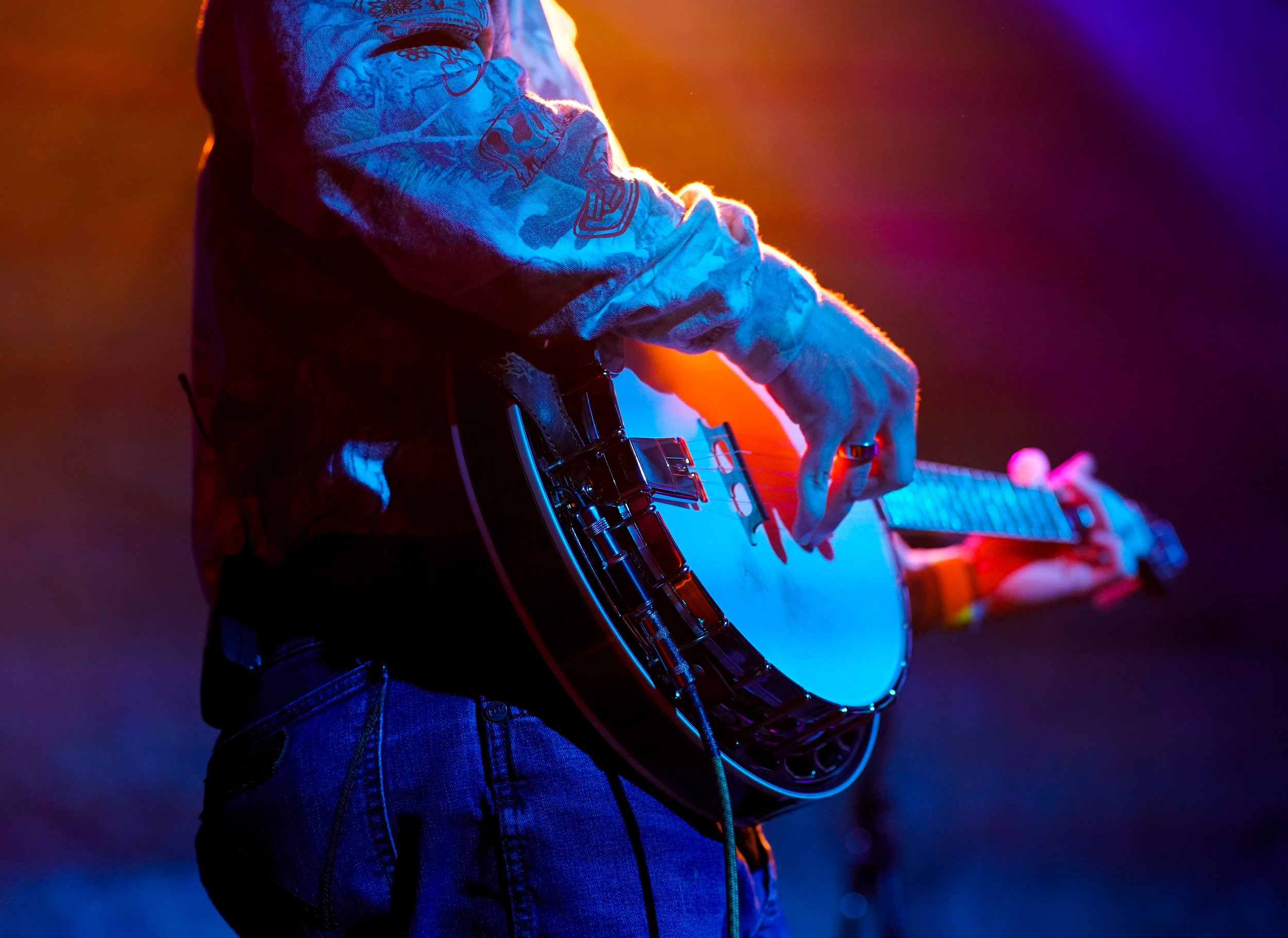 A person playing an electric guitar on stage, illuminated by colorful stage lights.