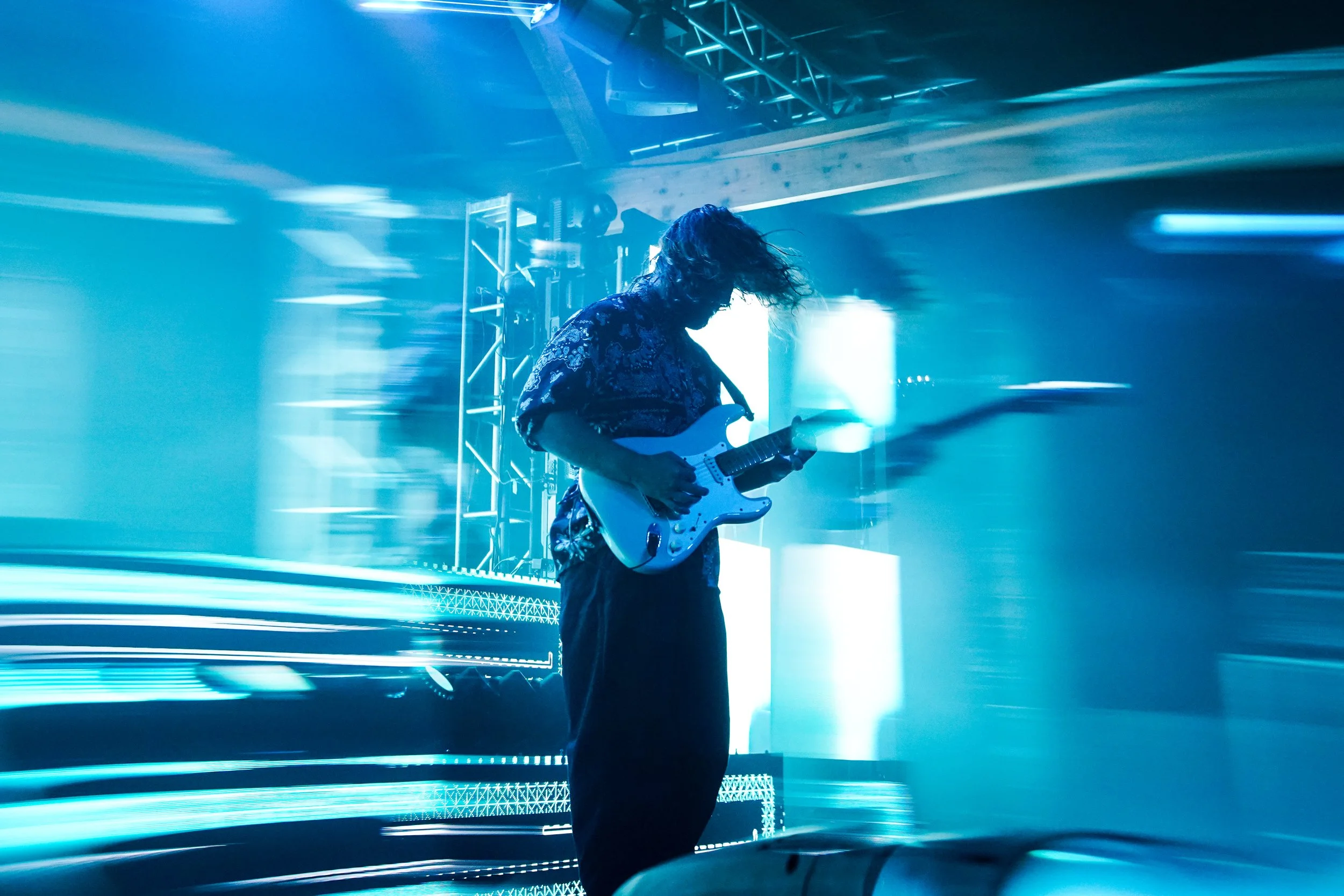 A person playing an electric guitar on stage with blue lighting and motion blur effects.