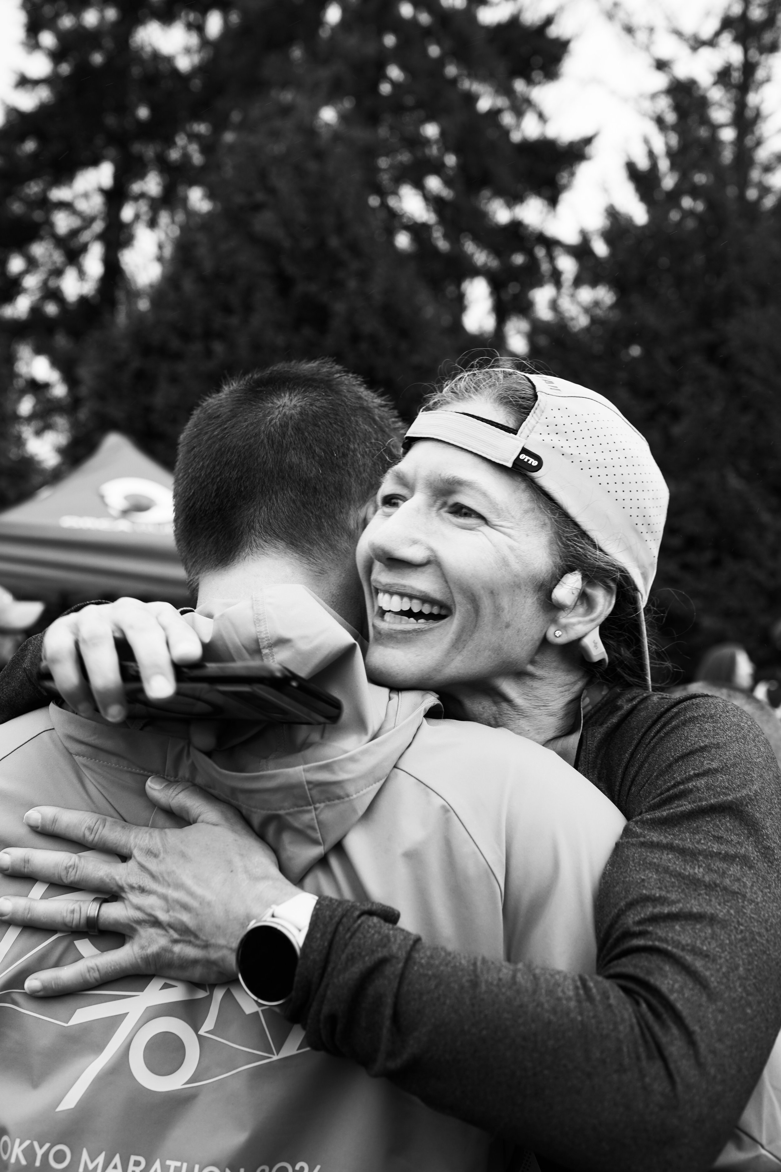 A woman in athletic clothing and a cap hugging a man after a marathon, smiling.