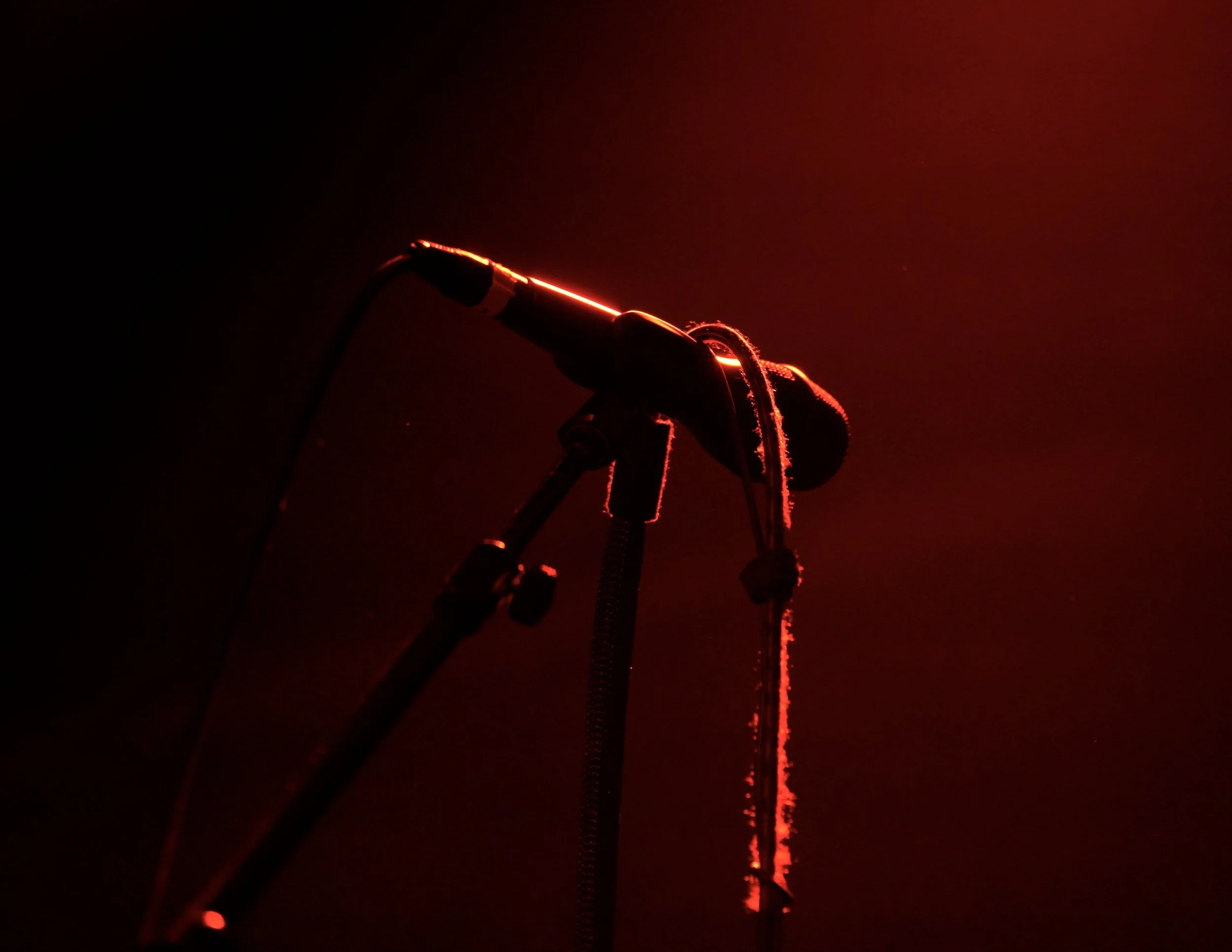 A close-up of a microphone with red LED lights, mounted on a stand against a dark background.