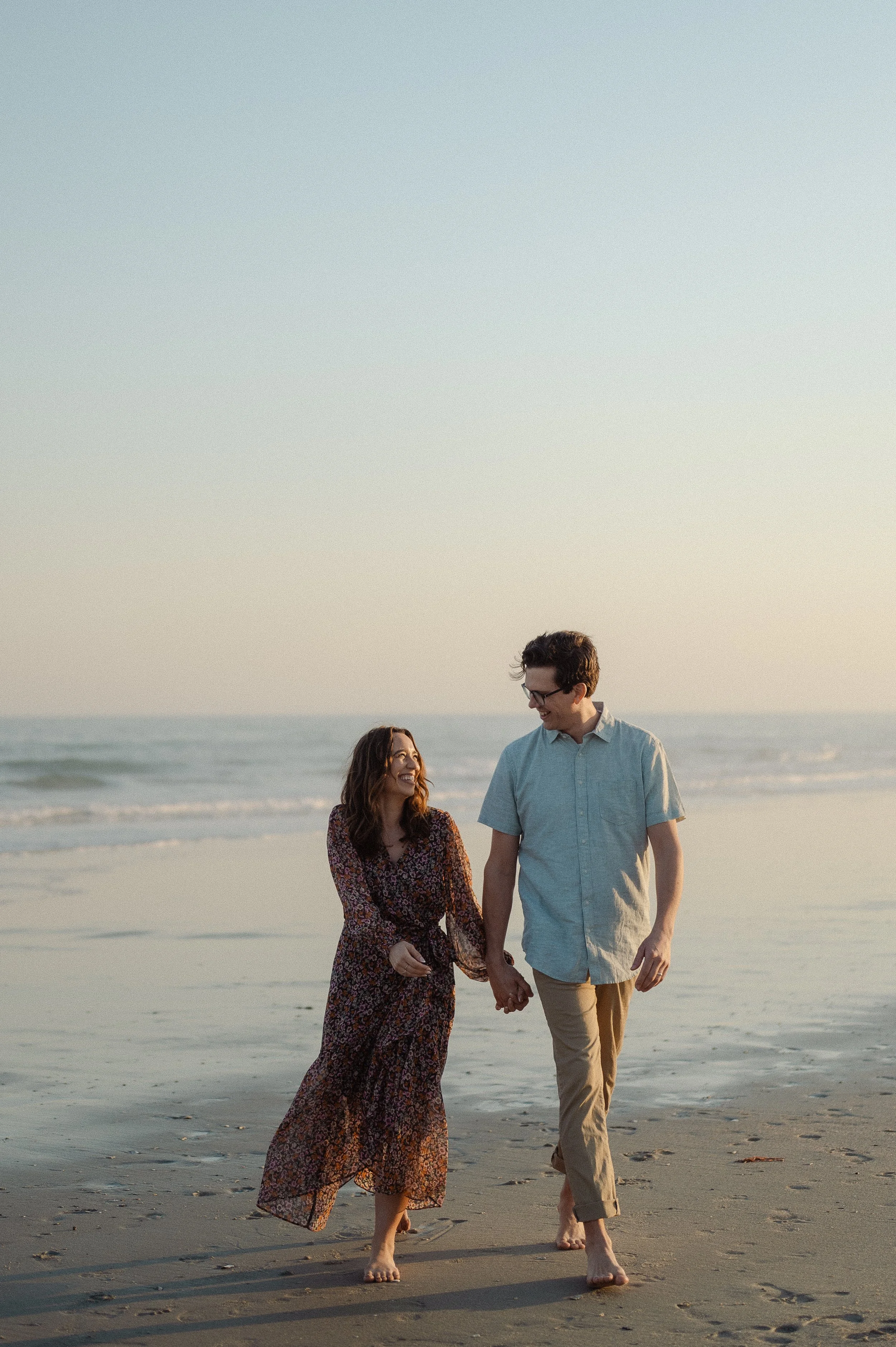 Author Kayla Craig has been married to her husband Jonny for more than 18 years. They are holding hands and walking on the beach during sunset, smiling and looking at each other.