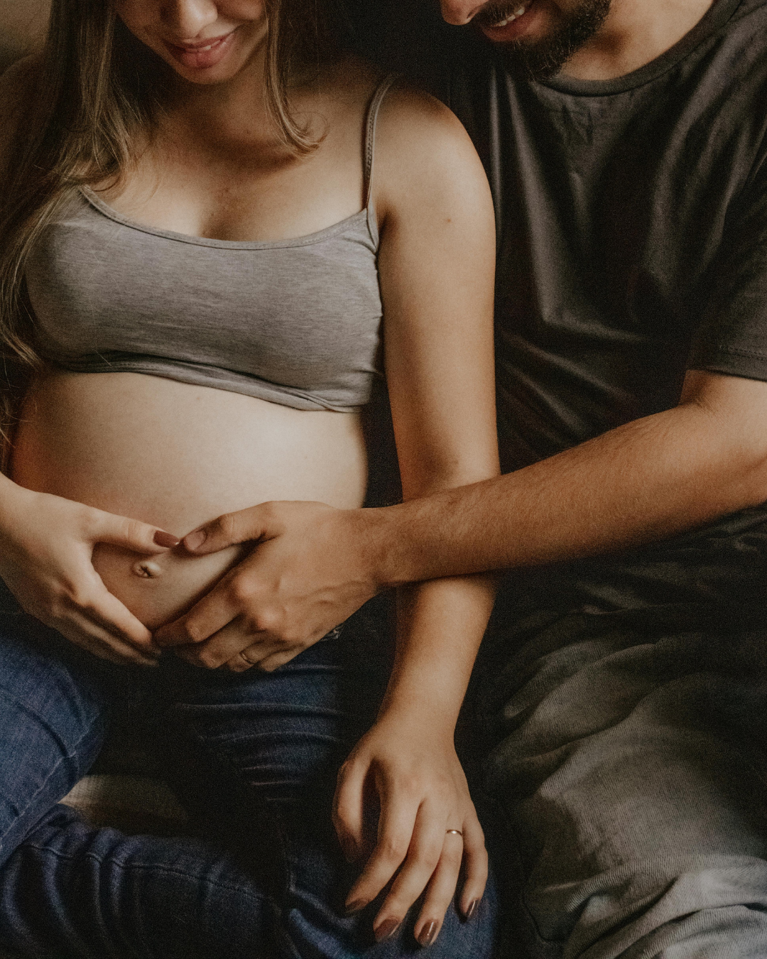 A couple sitting close, with hands on a pregnant woman's belly, smiling gently.