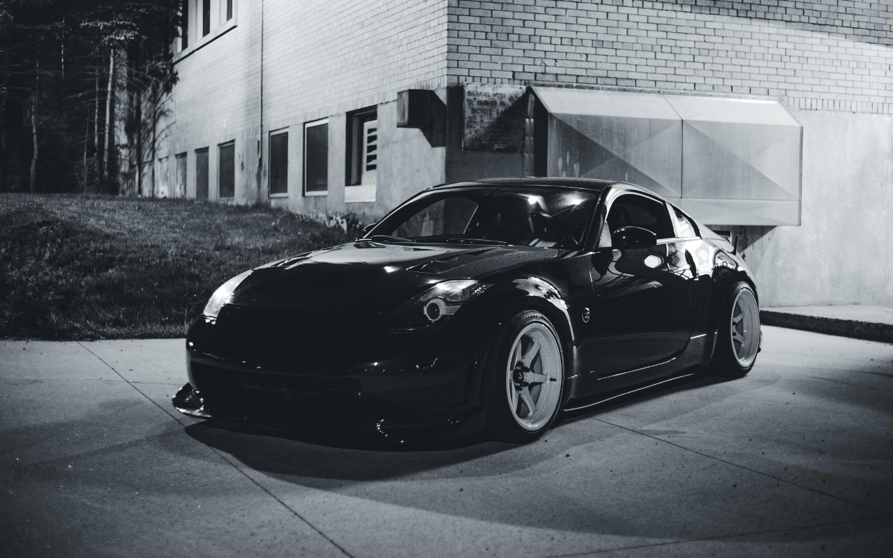 A black sports car parked on a street at night, with a brick building and windows in the background.