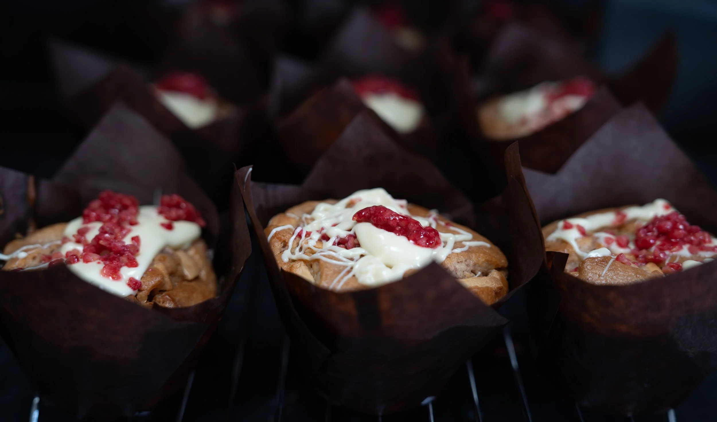 Assorted muffins topped with white icing and red crumbs, placed in dark brown paper liners.