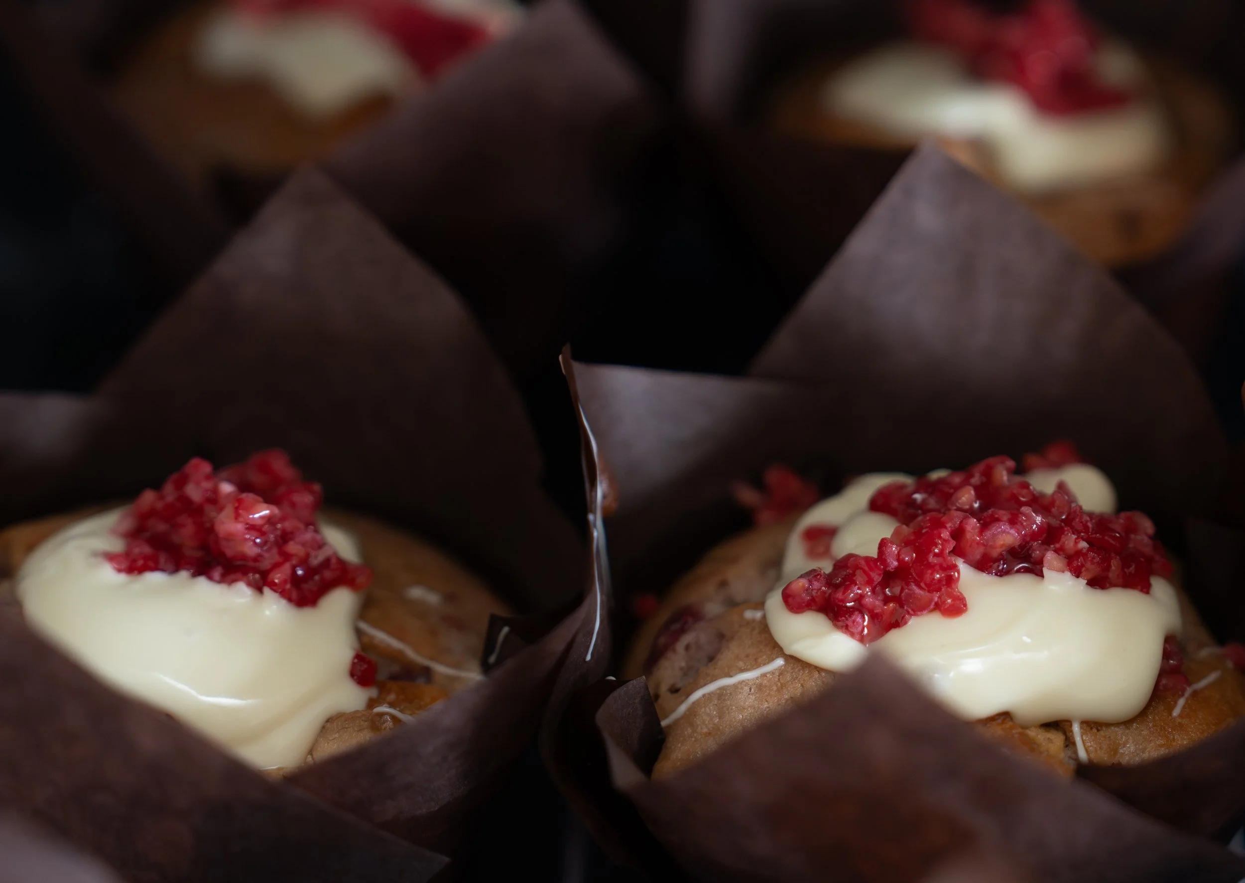 Close-up of decorated mini cupcakes with white frosting and red topping, surrounded by dark chocolate wrappers.