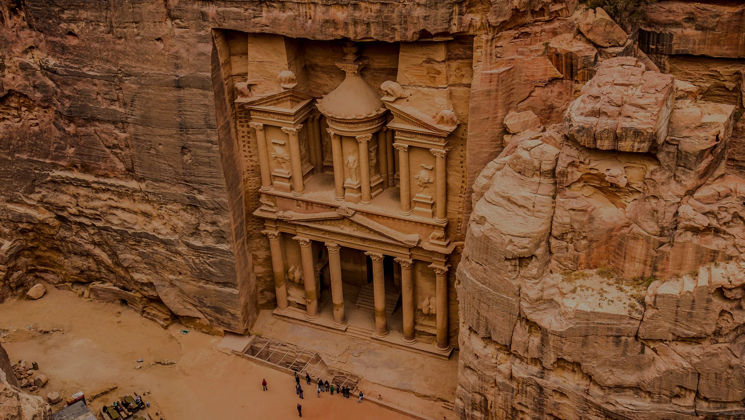 A breathtaking view of the ancient Al-Khazneh (The Treasury) carved into the red sandstone cliffs of Petra, Jordan, seen through the narrow opening of the Siq canyon.