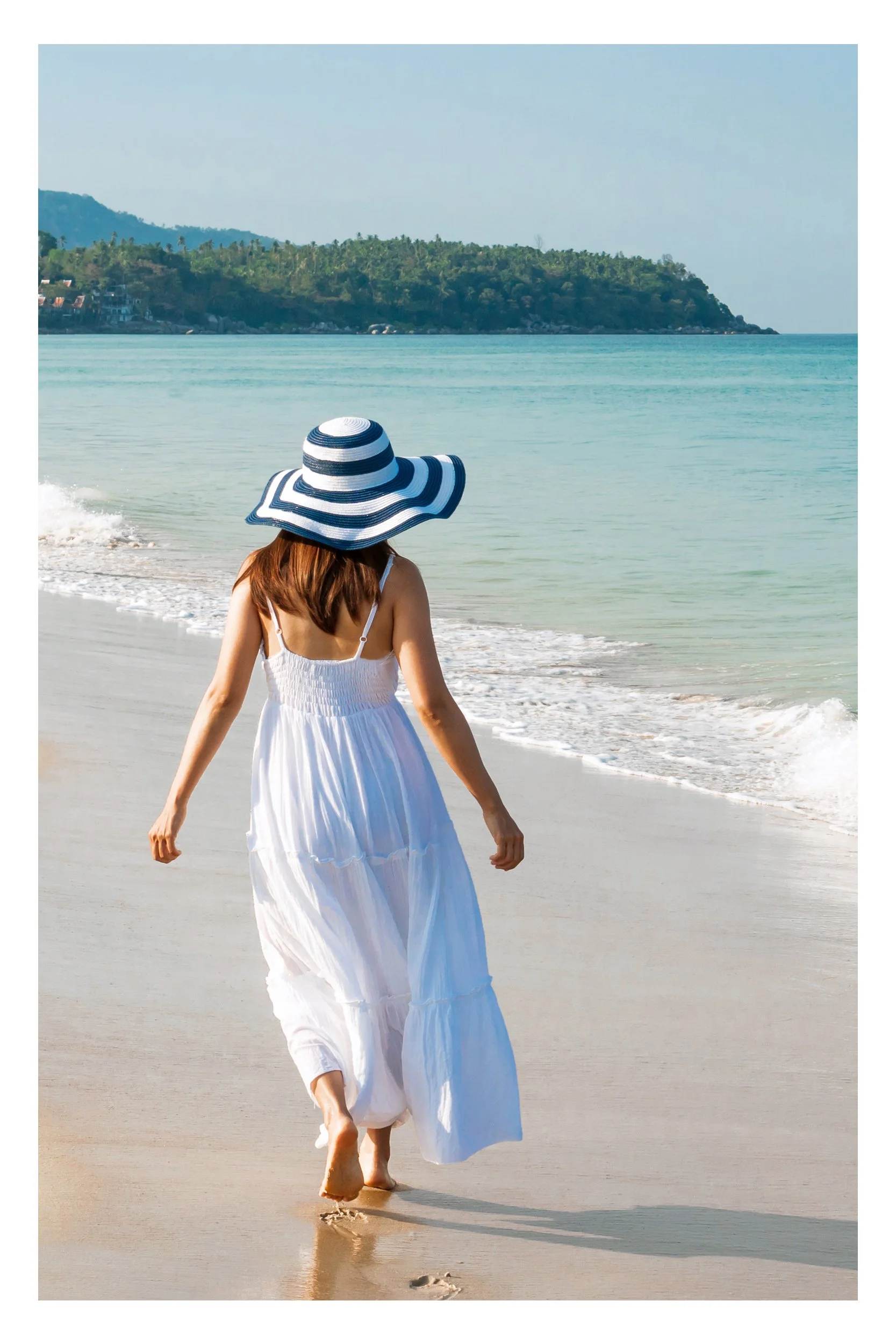 A woman walking peacefully along a secluded white sand beach with calm, crystal-clear turquoise water in a tropical paradise.