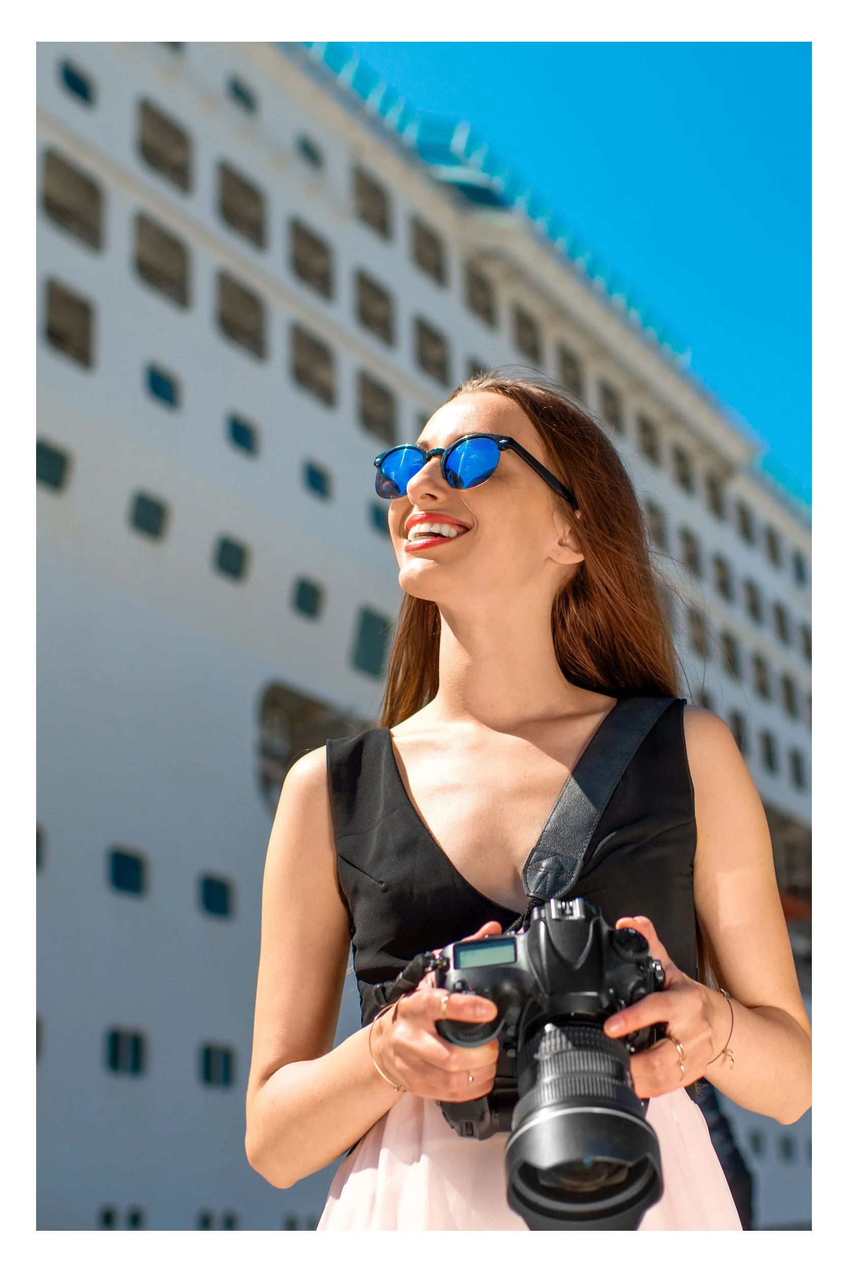 A woman standing on a pier in front of a large luxury cruise ship, holding a camera and ready to capture photos of her journey.