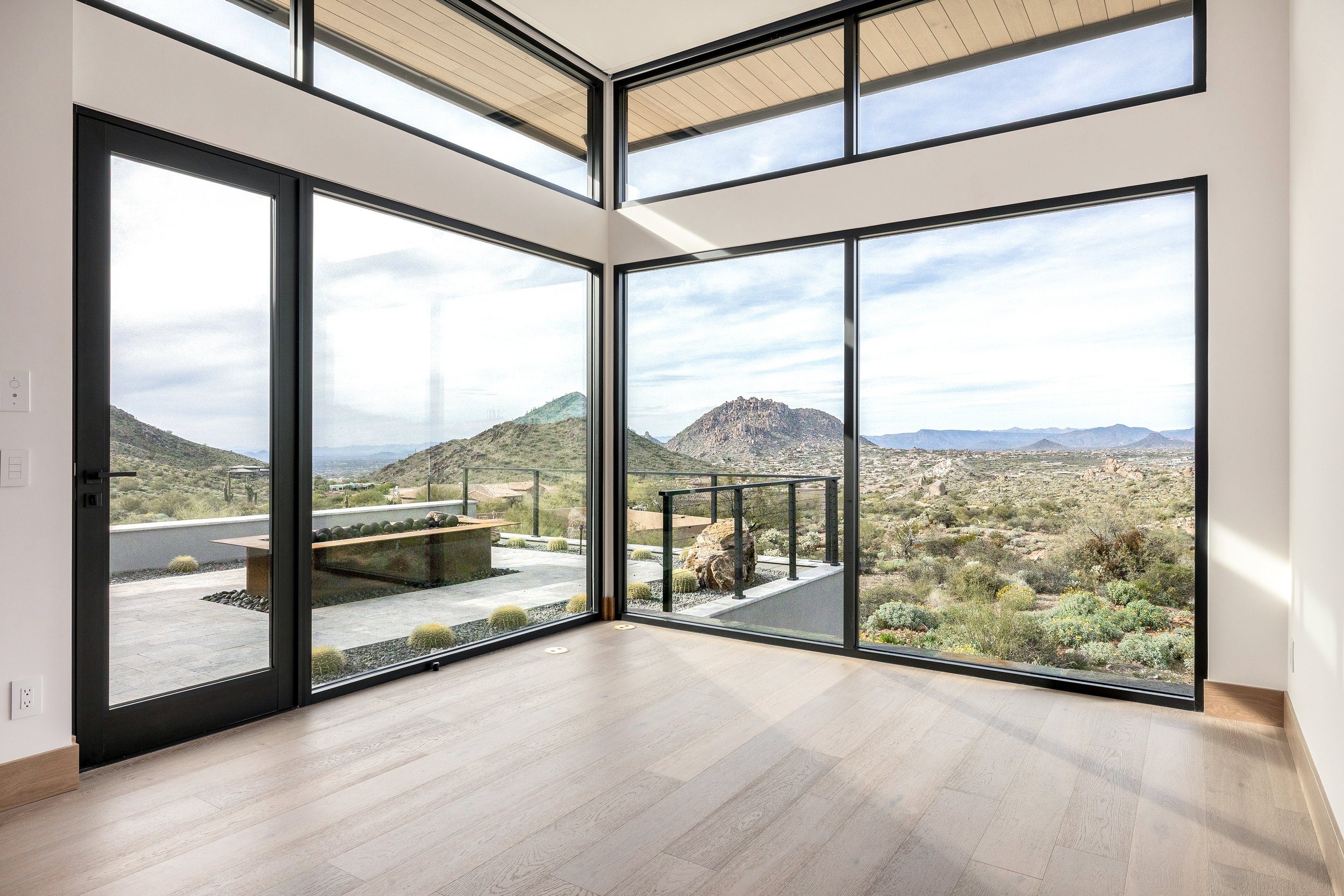 Modern living room with large floor-to-ceiling windows showing a desert landscape with mountains in the distance.