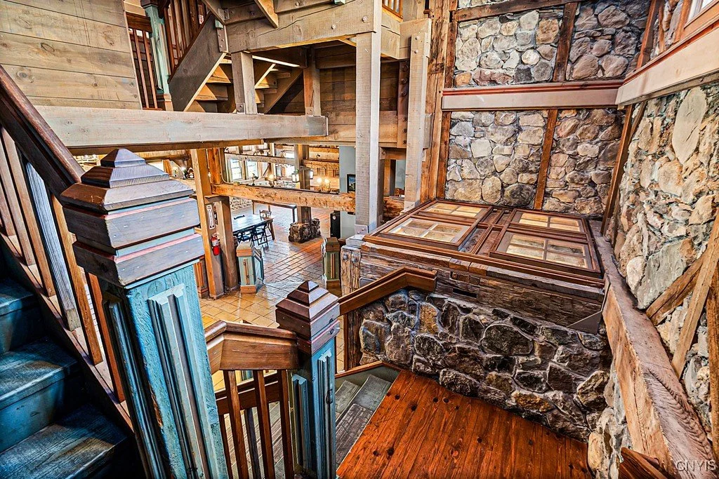 Interior view of a multi-level wooden cabin with stone accents, wooden staircases, and a cozy open layout, including a dining area and living space.