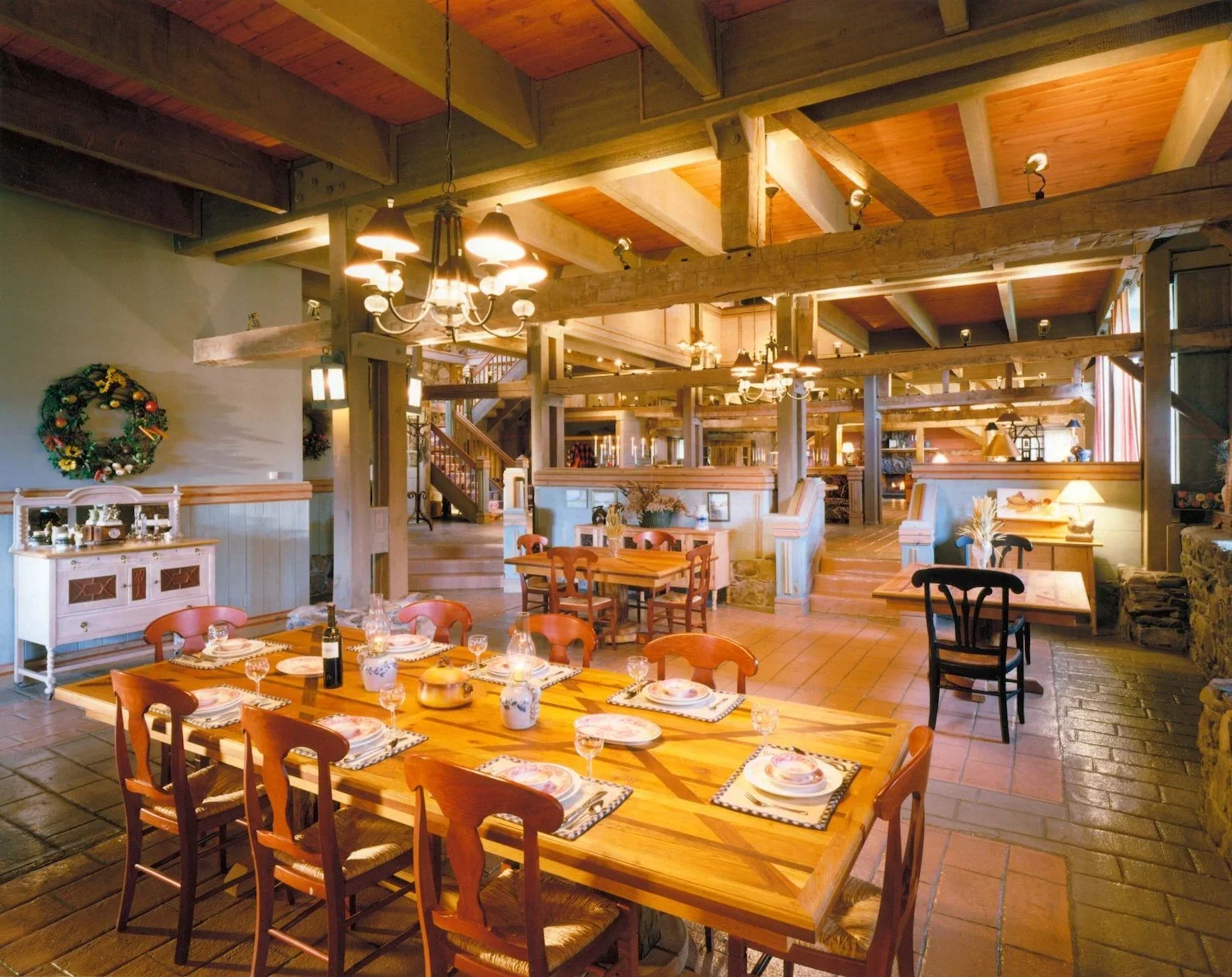 Interior of a cozy dining area decorated for Christmas with wooden furniture, a table set for eight, and festive wreaths on the wall.