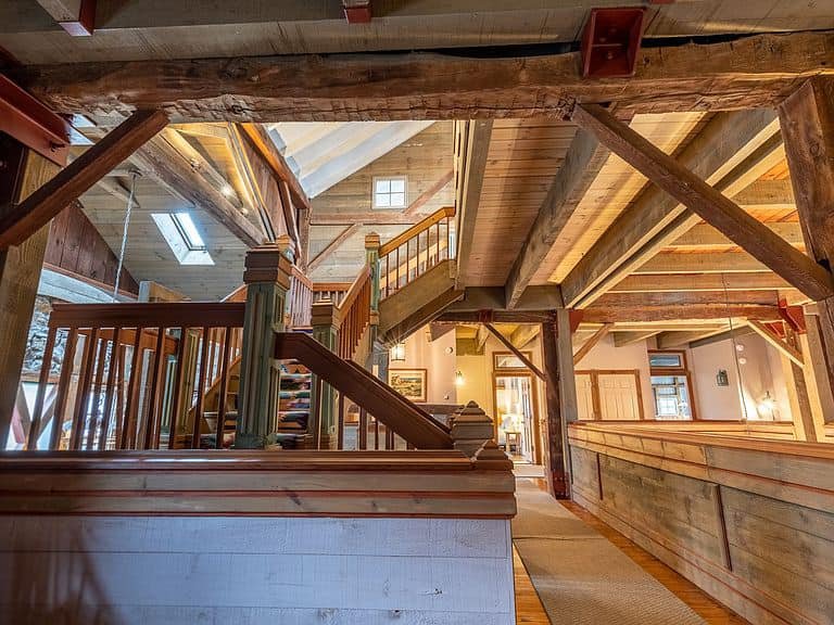 Interior view of a rustic wooden cabin with exposed beams, stairs, and natural light from windows.