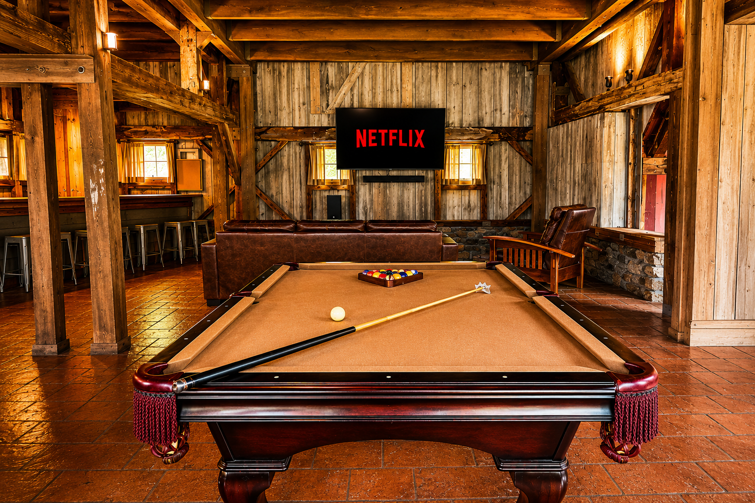 A rustic indoor game room featuring a pool table with a cue stick resting on it, a ball rack, and an off-white cue ball. In the background, a leather armchair and a sofa are situated in front of a wall-mounted flat-screen Netflix TV. The room has wooden walls, exposed beams, small windows with yellow curtains, and warm lighting.