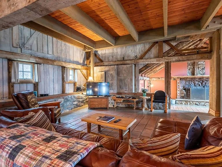 Rustic living room with leather couches, wooden walls, and a stone fireplace.