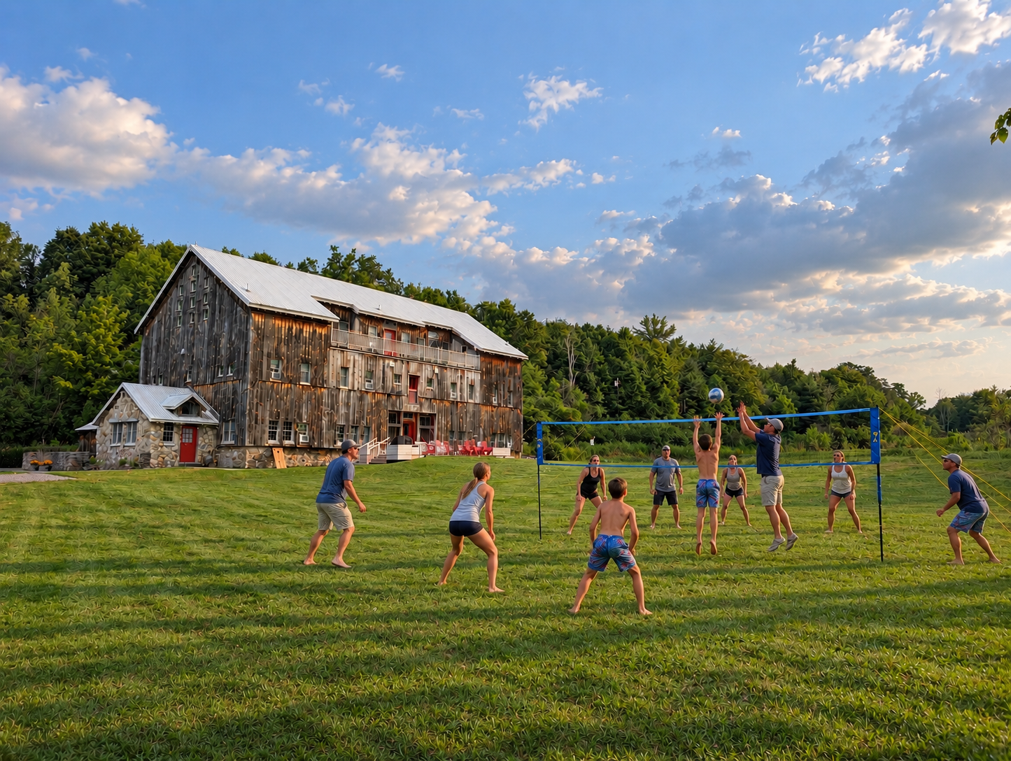People playing volleyball on a large grassy field near a rustic wooden building under a sky with scattered clouds.