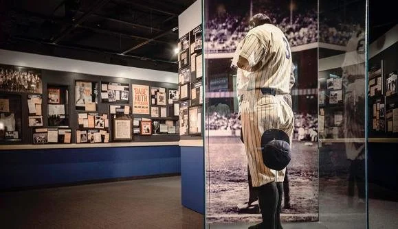 A museum exhibit showcasing a person in baseball uniform facing away, with display panels and memorabilia on the walls.