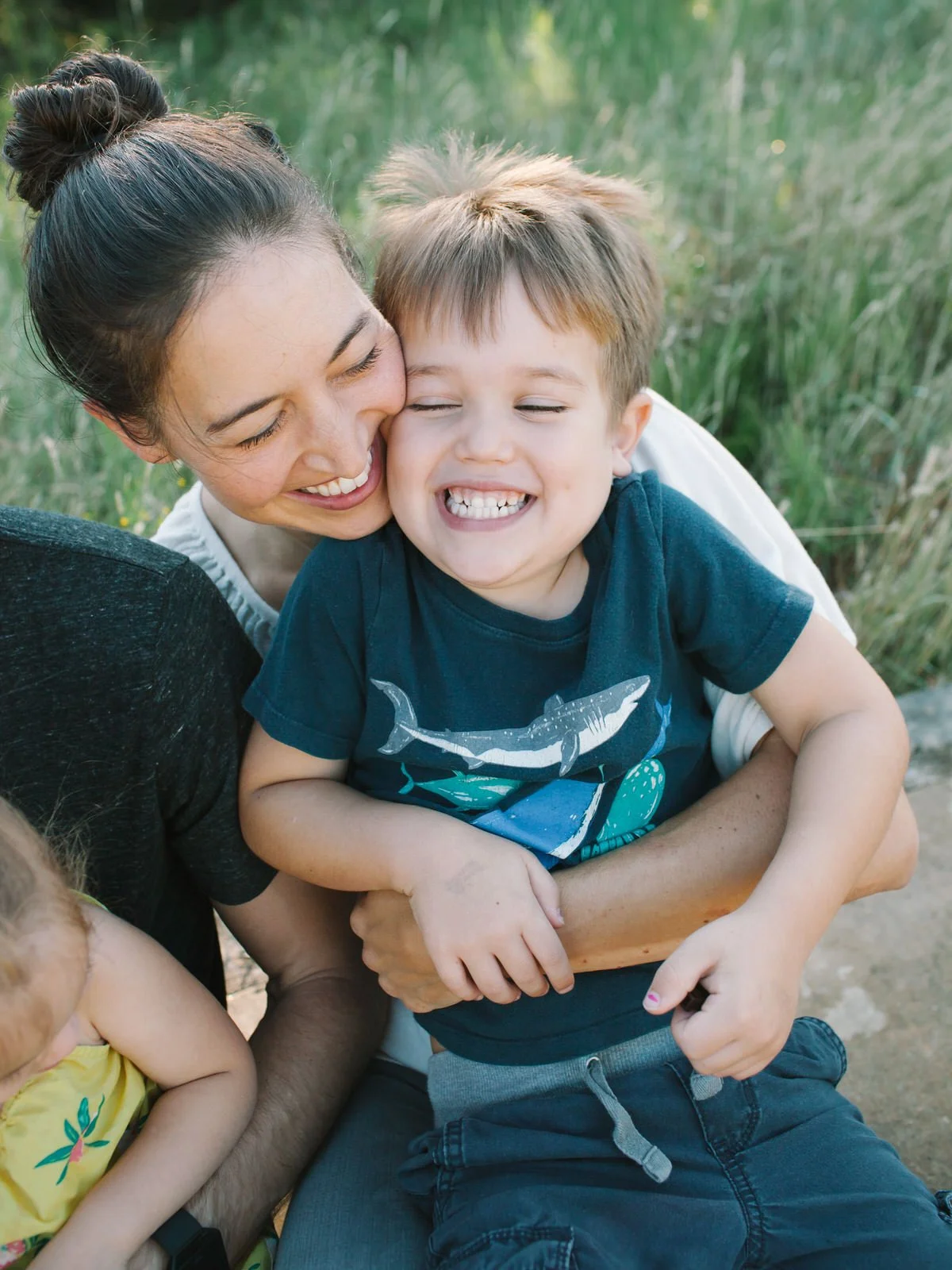 A woman and a young boy sharing a joyful moment outdoors, with the woman hugging the boy from behind and they both laughing.