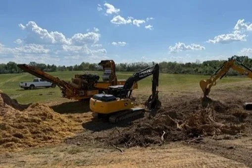 Construction site with excavators and a parked white truck in a grassy field under a blue sky with scattered clouds.