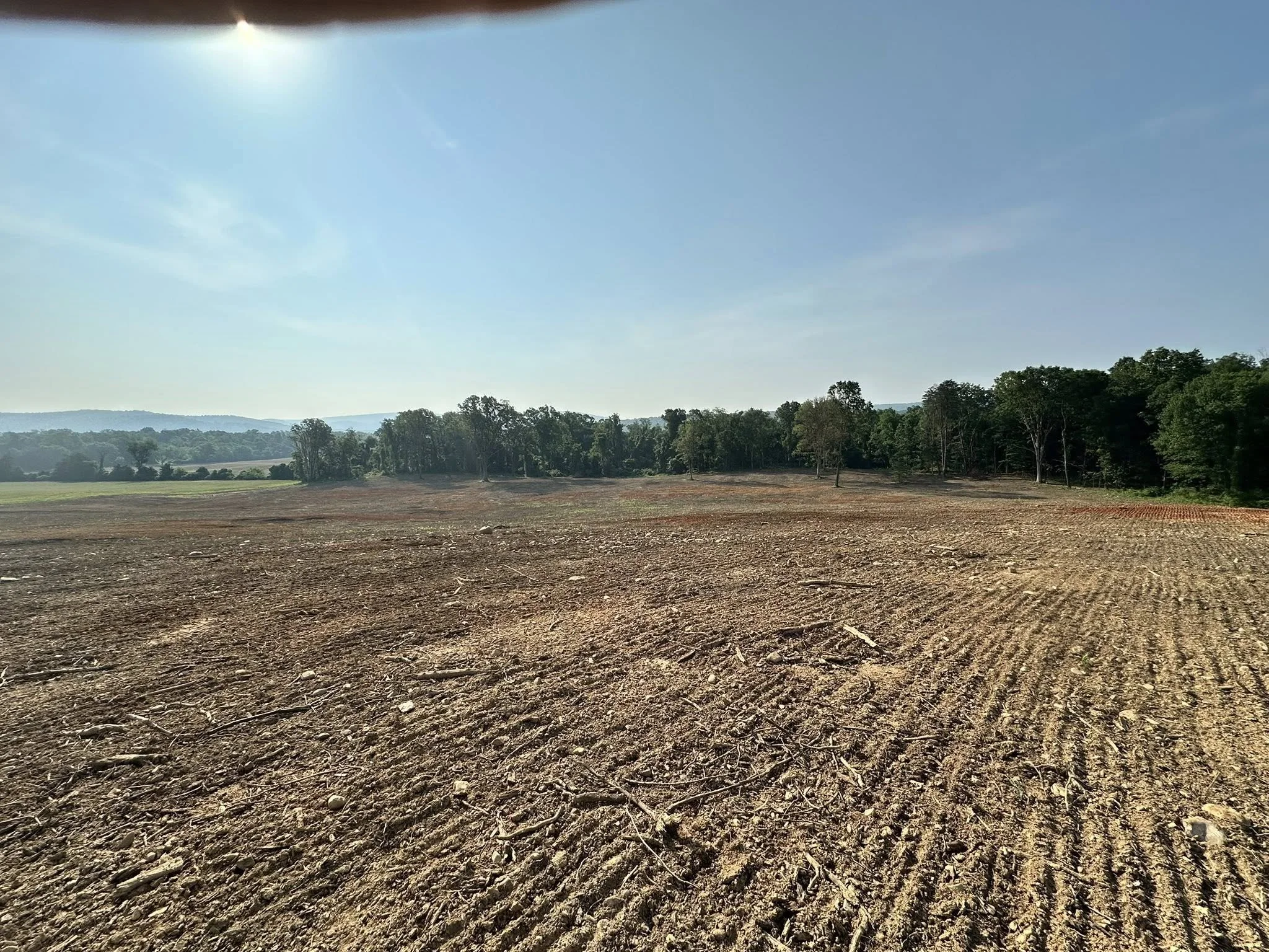 Photo of a freshly tilled dirt field with a line of trees in the background under a clear blue sky.