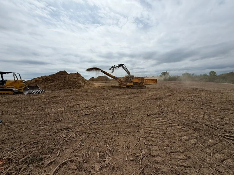 Construction site with excavator moving dirt, bulldozer on left, and cloudy sky.