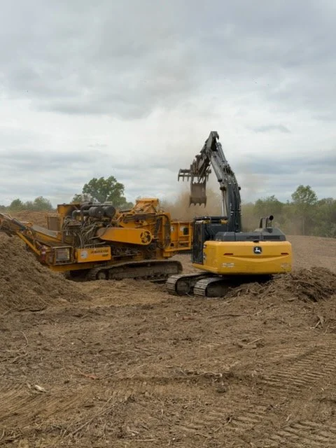 Construction site with a yellow bulldozer and a black excavator working on dirt under a cloudy sky.
