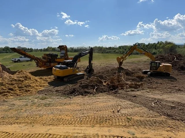 Construction site with two excavators digging in dirt, under a partly cloudy sky.