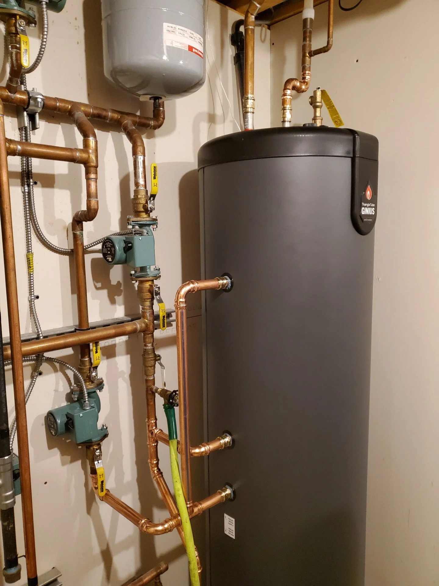 A water heater with various copper pipes, valves, and control units installed on a wall in a utility room.
