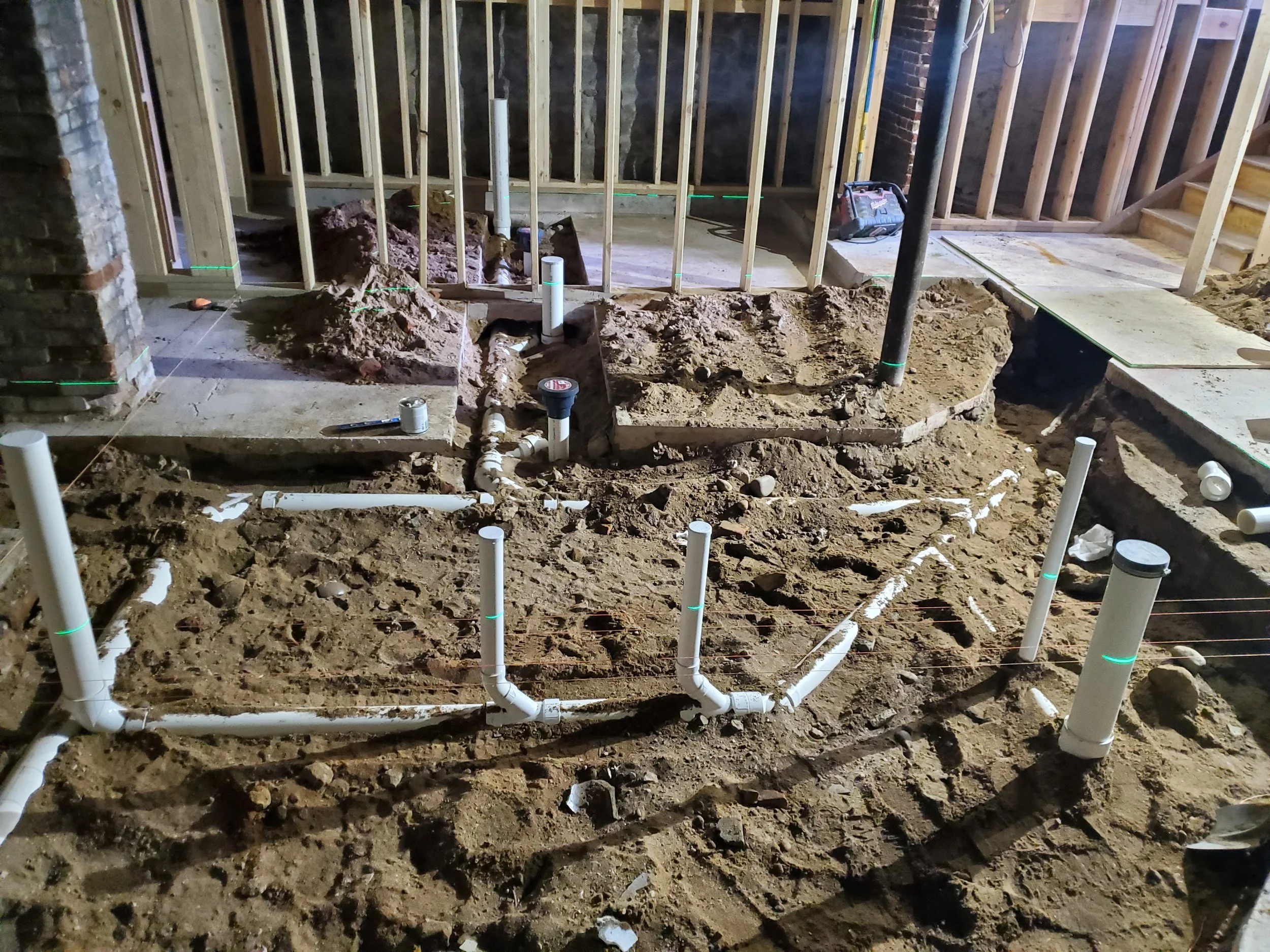 Construction site with exposed pipes and framing for a building renovation or addition, including a partially completed staircase in the background.