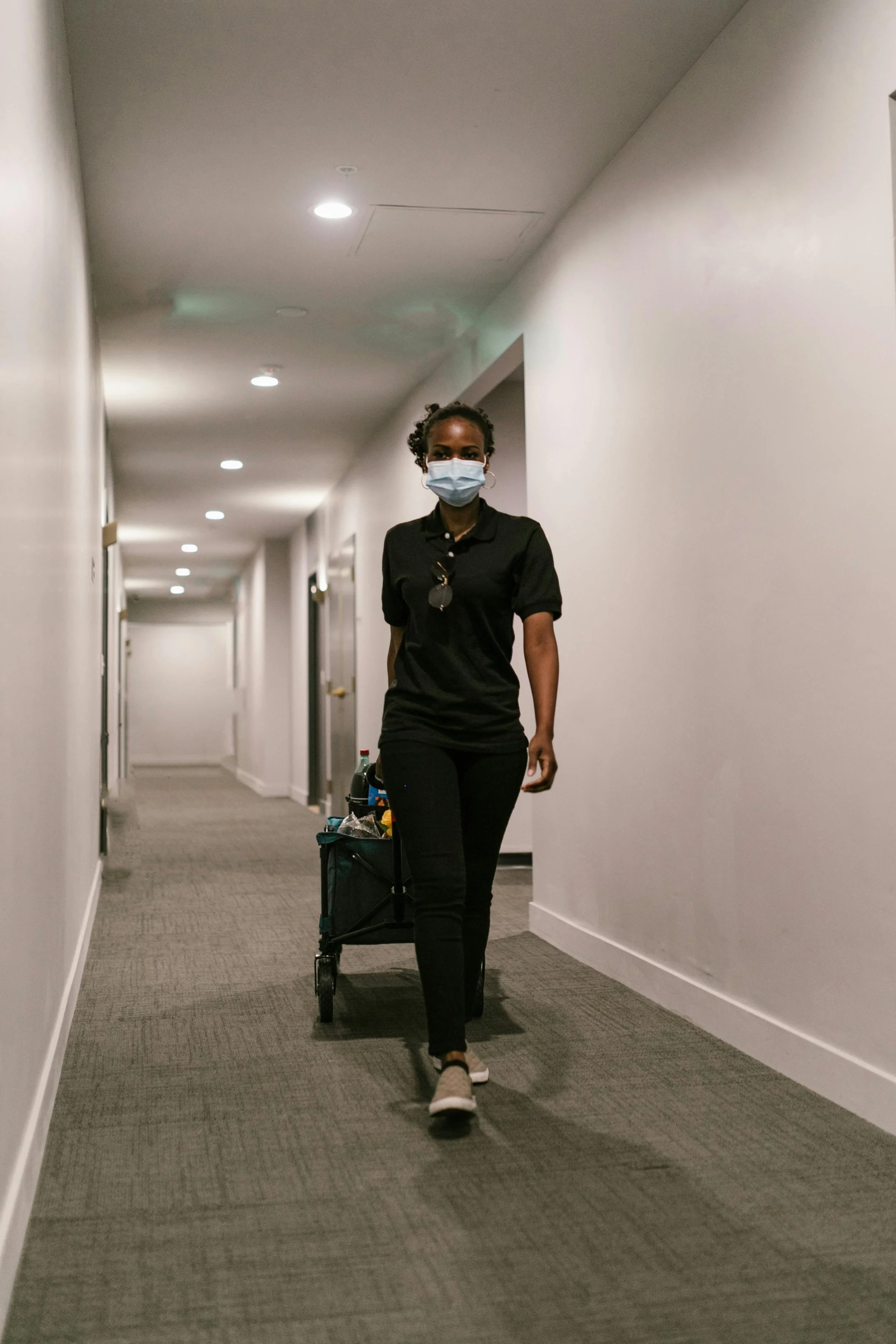 Professional day porter pulling cleaning equipment through a commercial facility hallway.