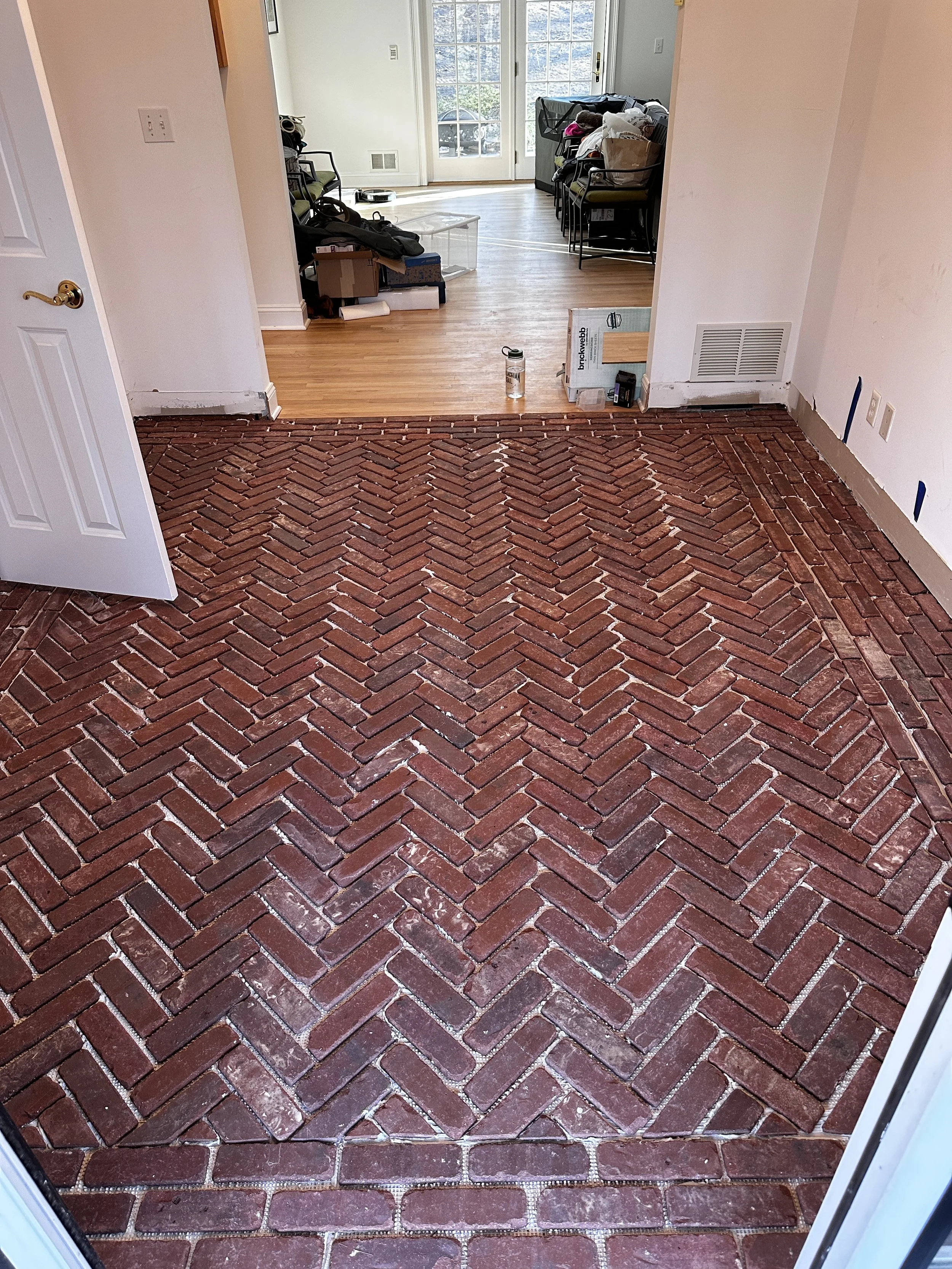 View from a doorway showing a room with a freshly laid brick herringbone pattern floor, with construction tools and materials nearby.