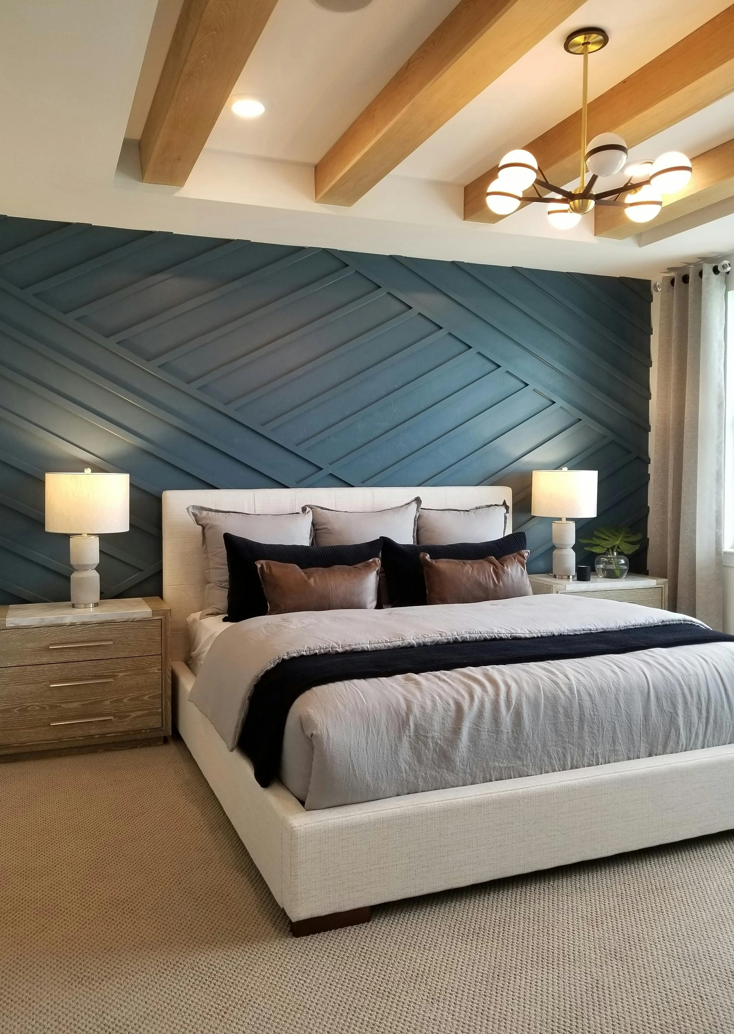 Modern bedroom featuring a white bed with multiple pillows, dark accent wall with wood paneling, two bedside tables with lamps, a ceiling light fixture, and a window with curtains.